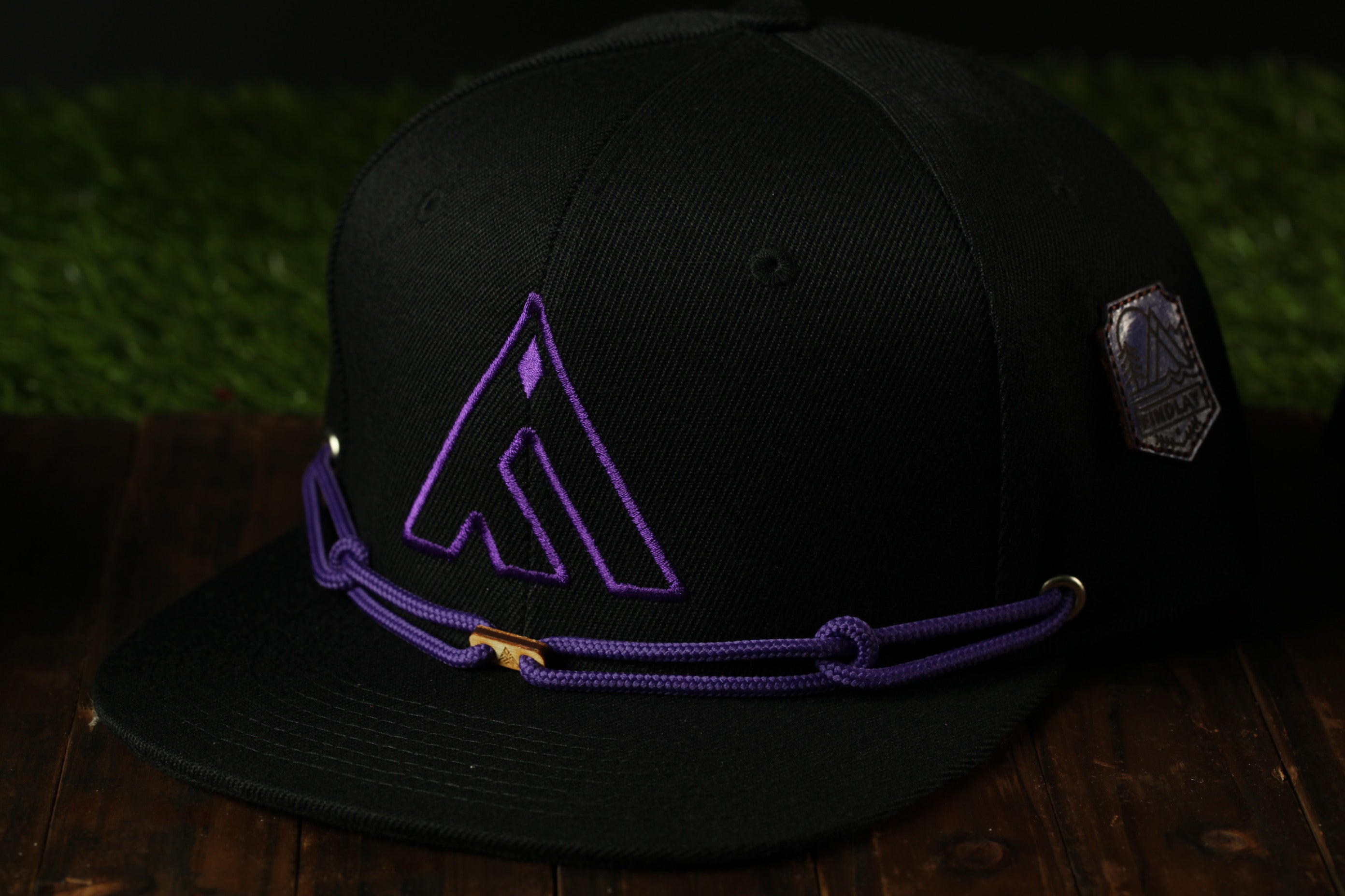 A black baseball cap with a purple logo on it, placed on a wooden surface.