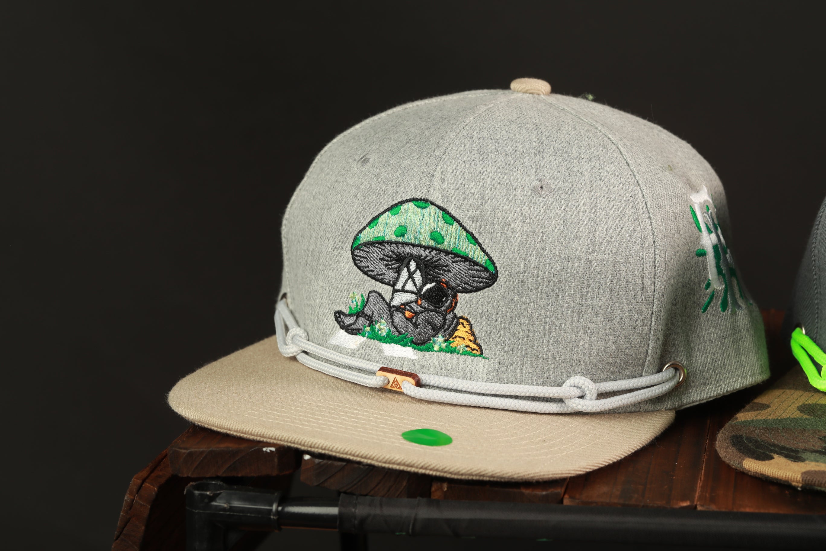 A gray baseball cap with a mushroom design and a green tag on the front, sitting on a wooden surface.