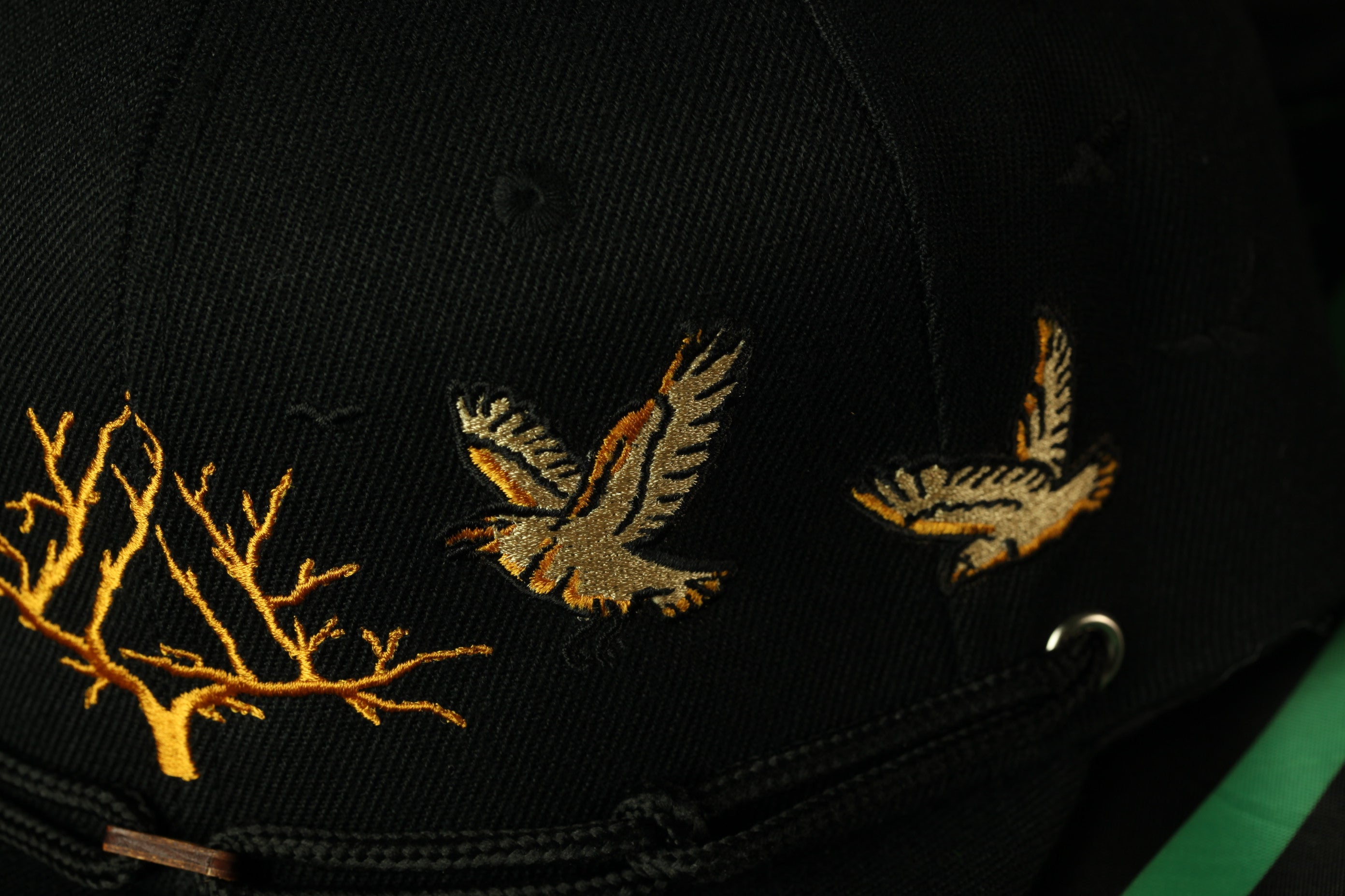 A close-up view of a black baseball cap with gold embroidered designs, including a branch and two birds.