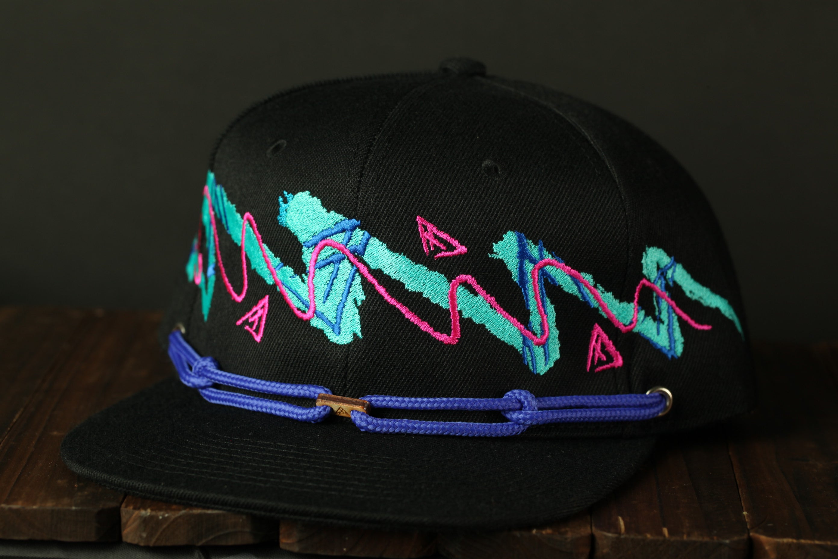 A black baseball cap with a colorful, abstract embroidered design on the front.
