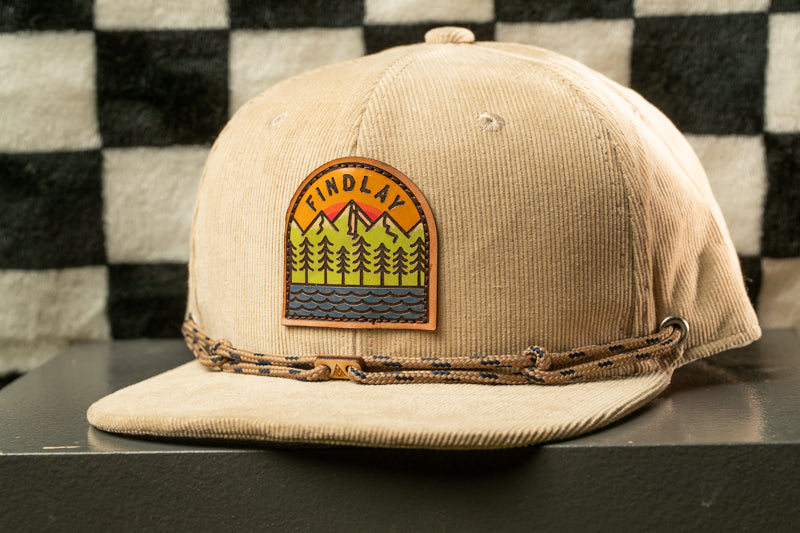 A beige baseball cap with a patch on the front, featuring a mountain landscape design.