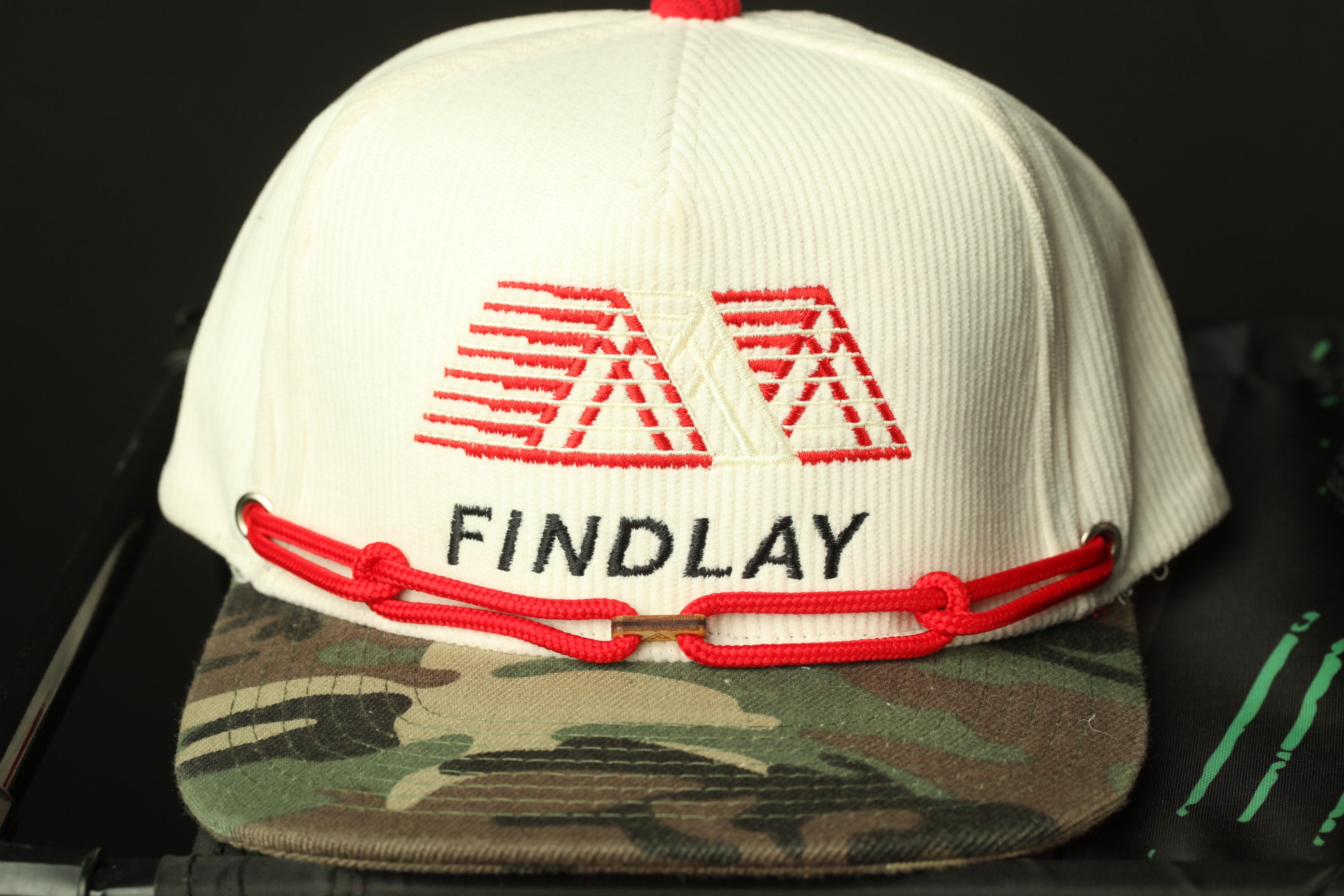 A white baseball cap with a red and black logo, featuring the word "FINDLAY" printed on it.