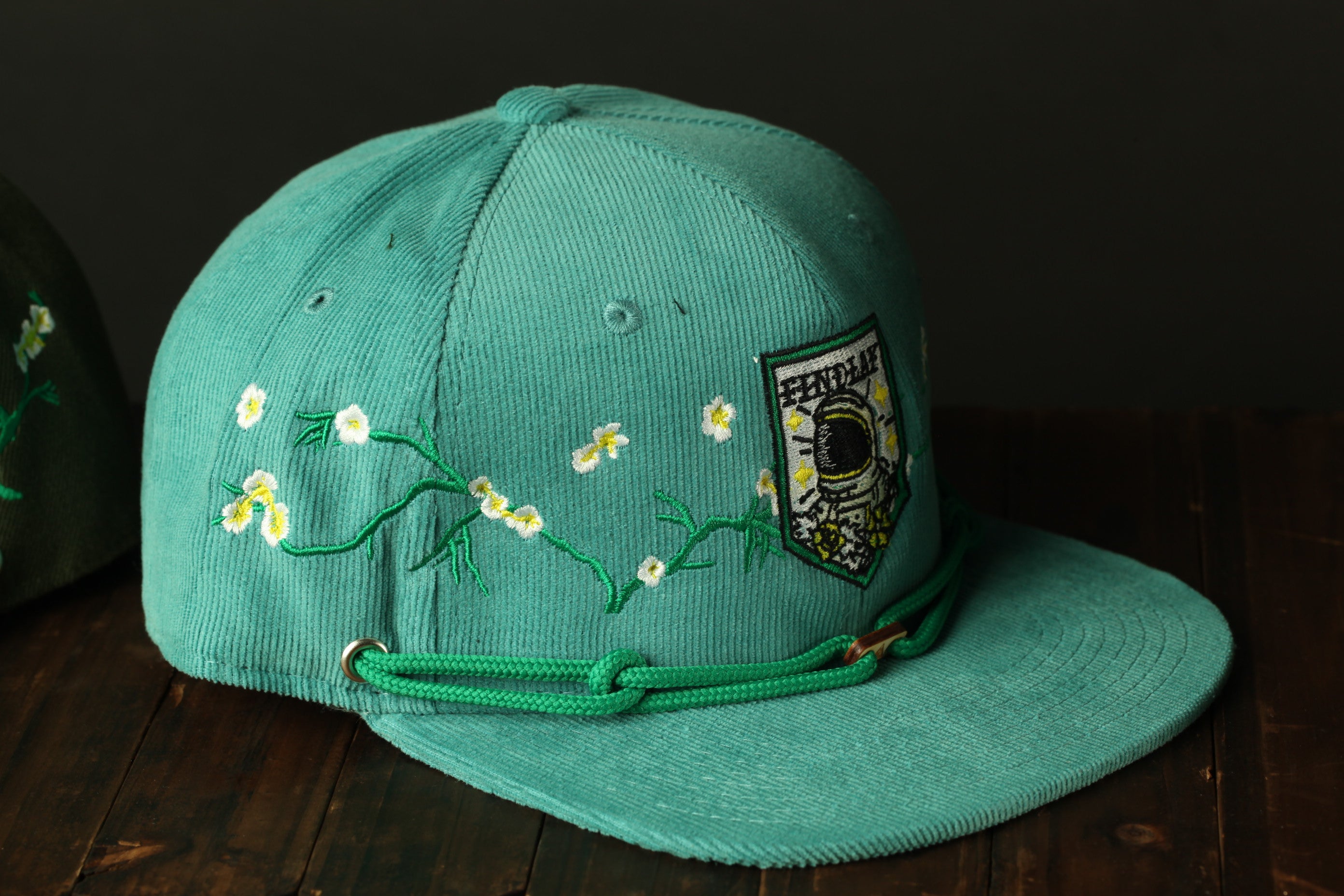 A turquoise baseball cap with a floral design and a patch on the front, sitting on a wooden surface.