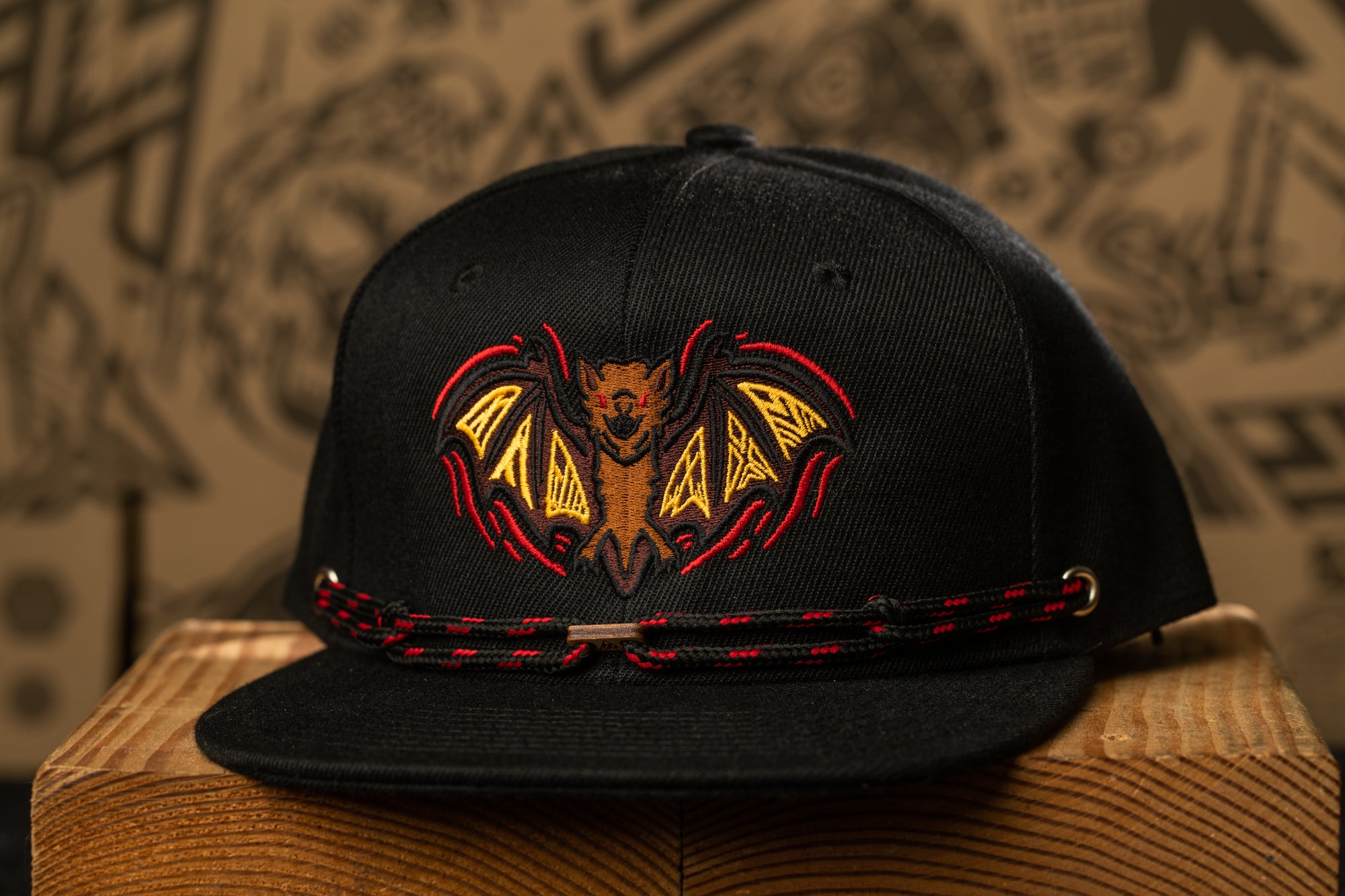 A black baseball cap with a bat design on the front, placed on a wooden surface against a background with abstract patterns.