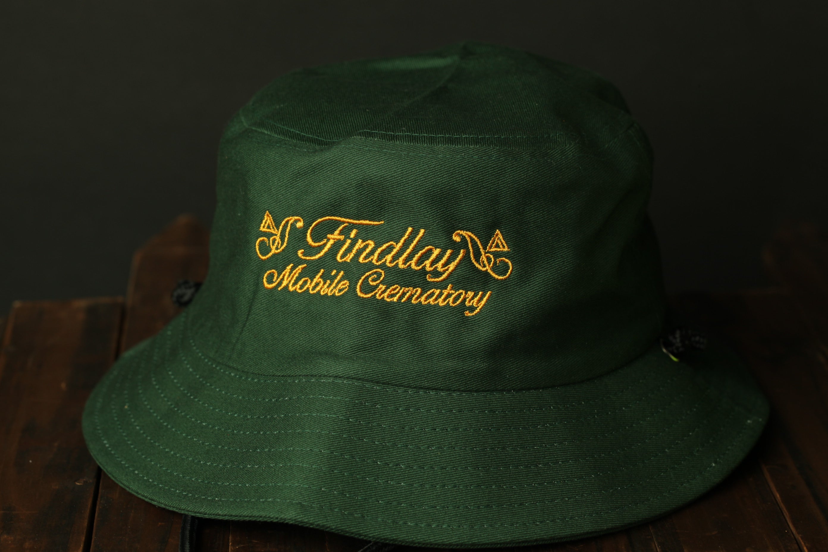 A green bucket hat with gold embroidered text on the front.