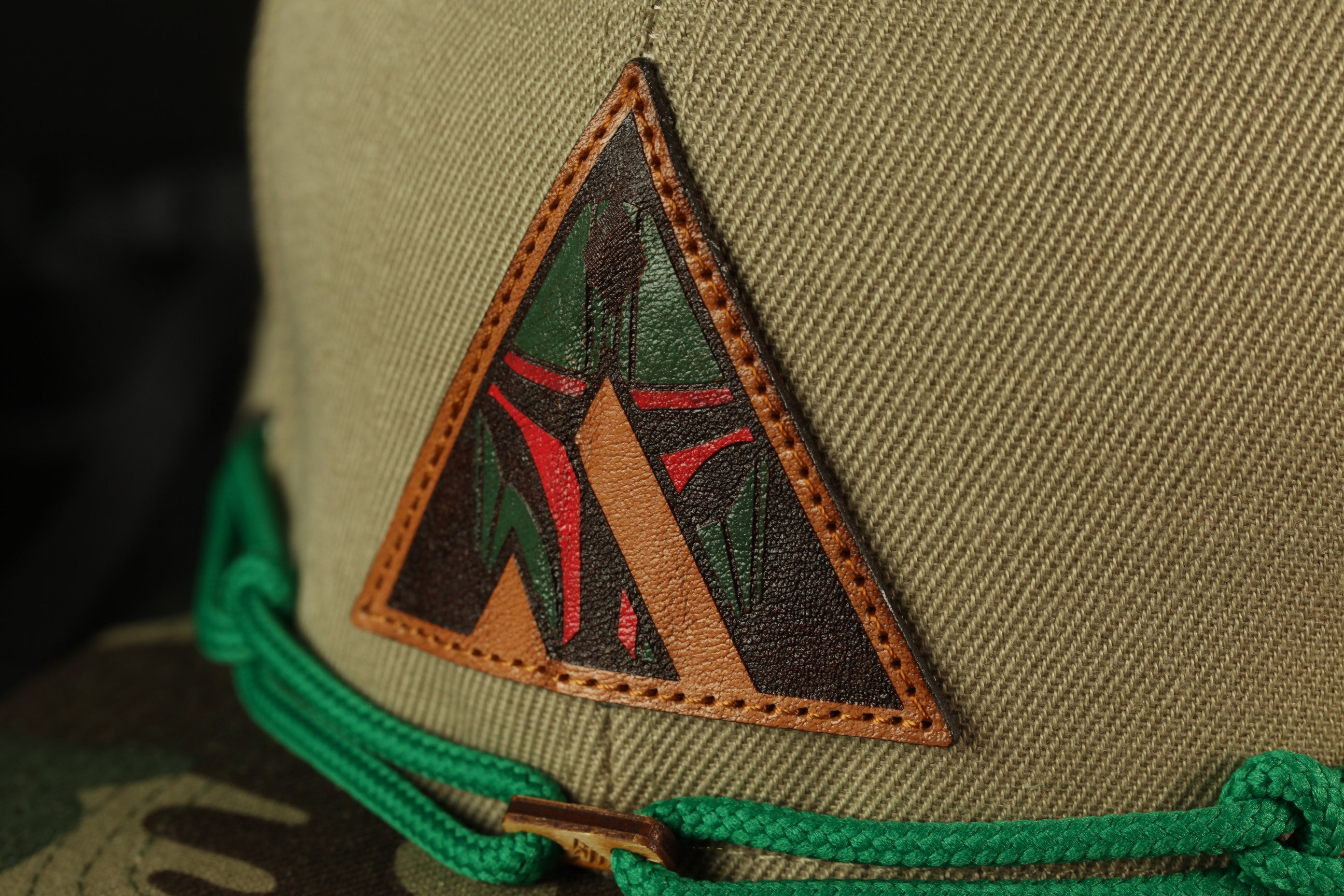 A close-up view of a beige fabric with a triangular patch featuring a red and green design, attached to a green string.