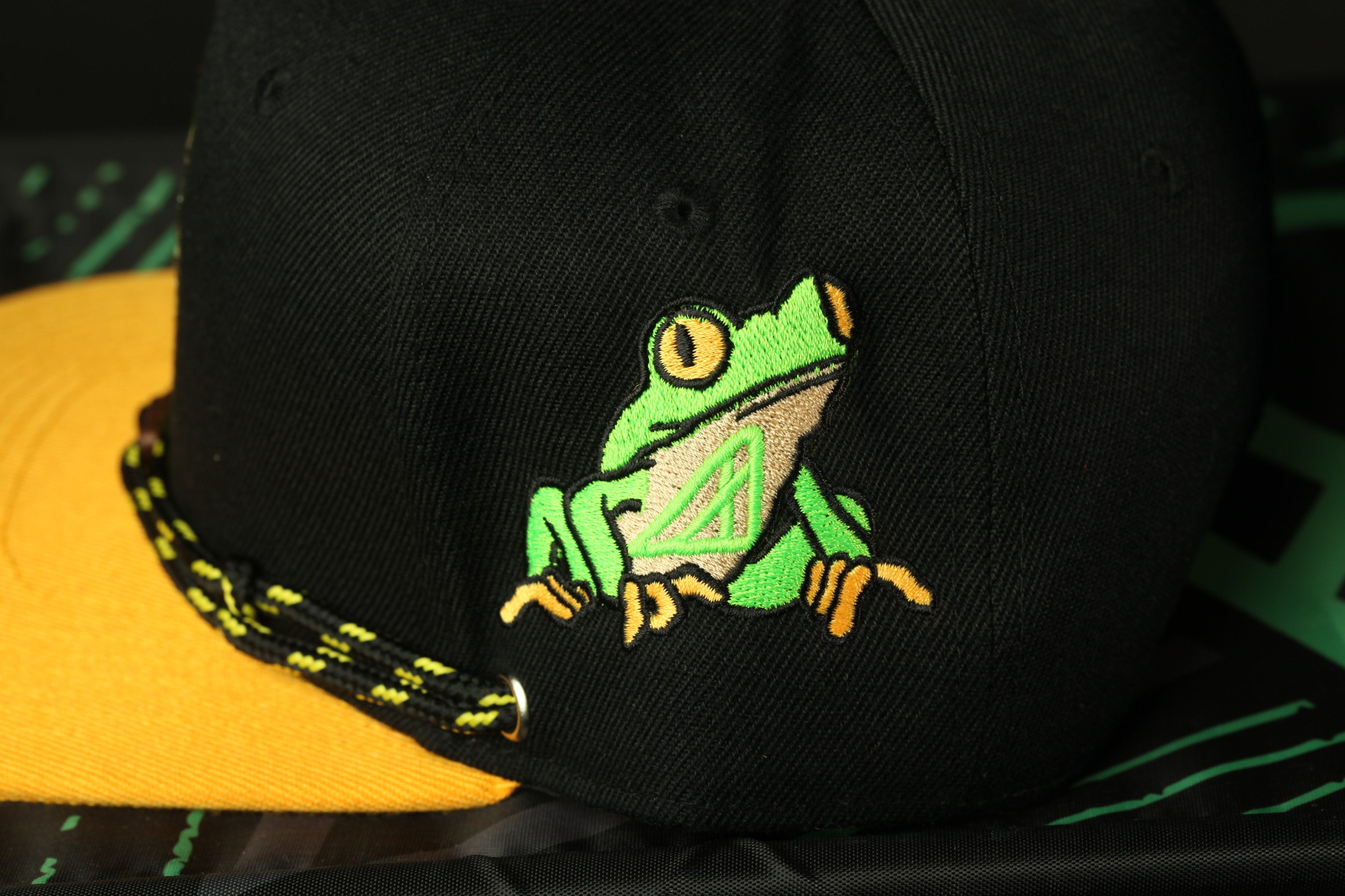 A close-up view of a black baseball cap with a green frog embroidered on it.