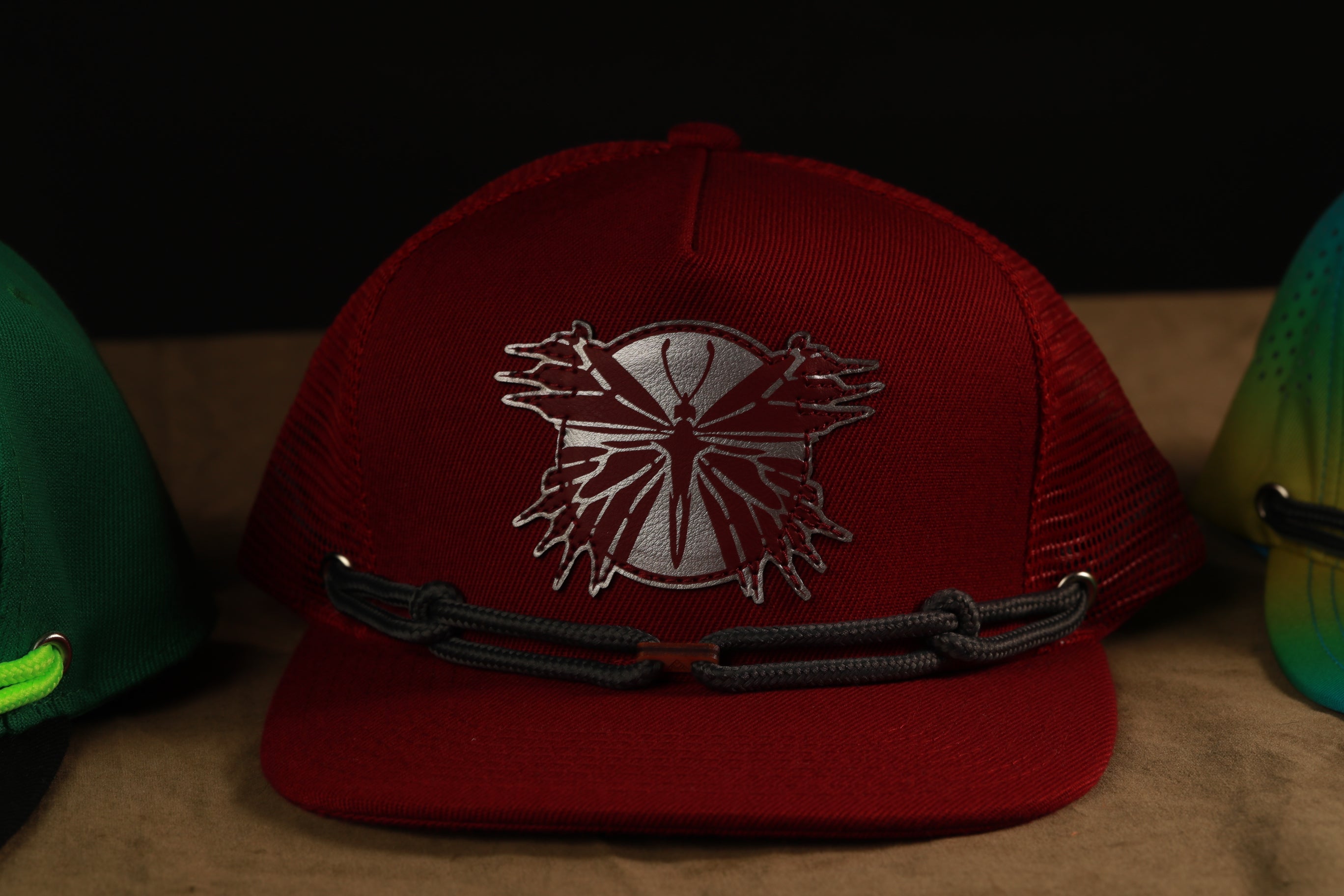 A red baseball cap with a silver butterfly design on the front, sitting on a surface with other hats in the background.