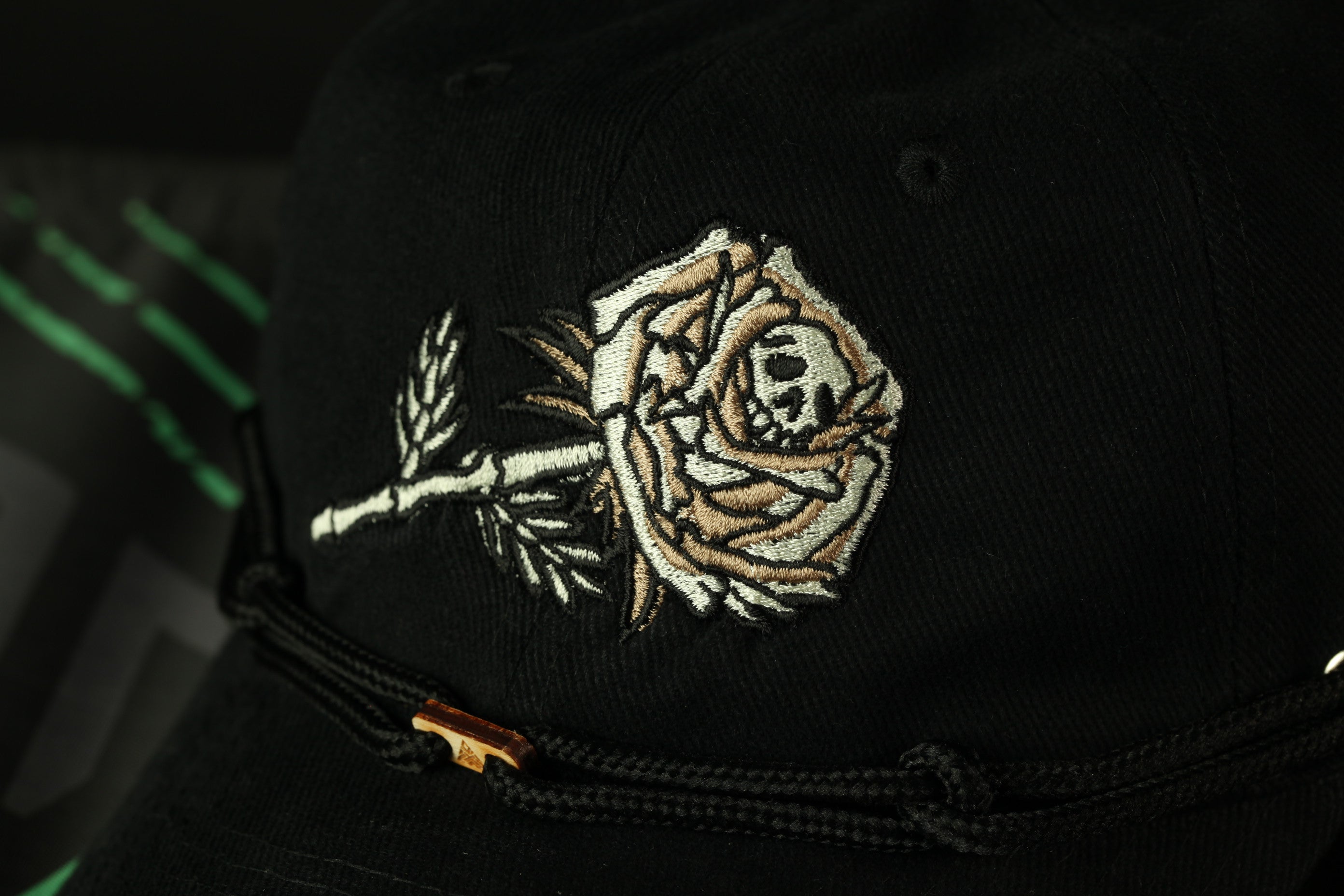 A close-up view of a black baseball cap with an embroidered rose design on the front.