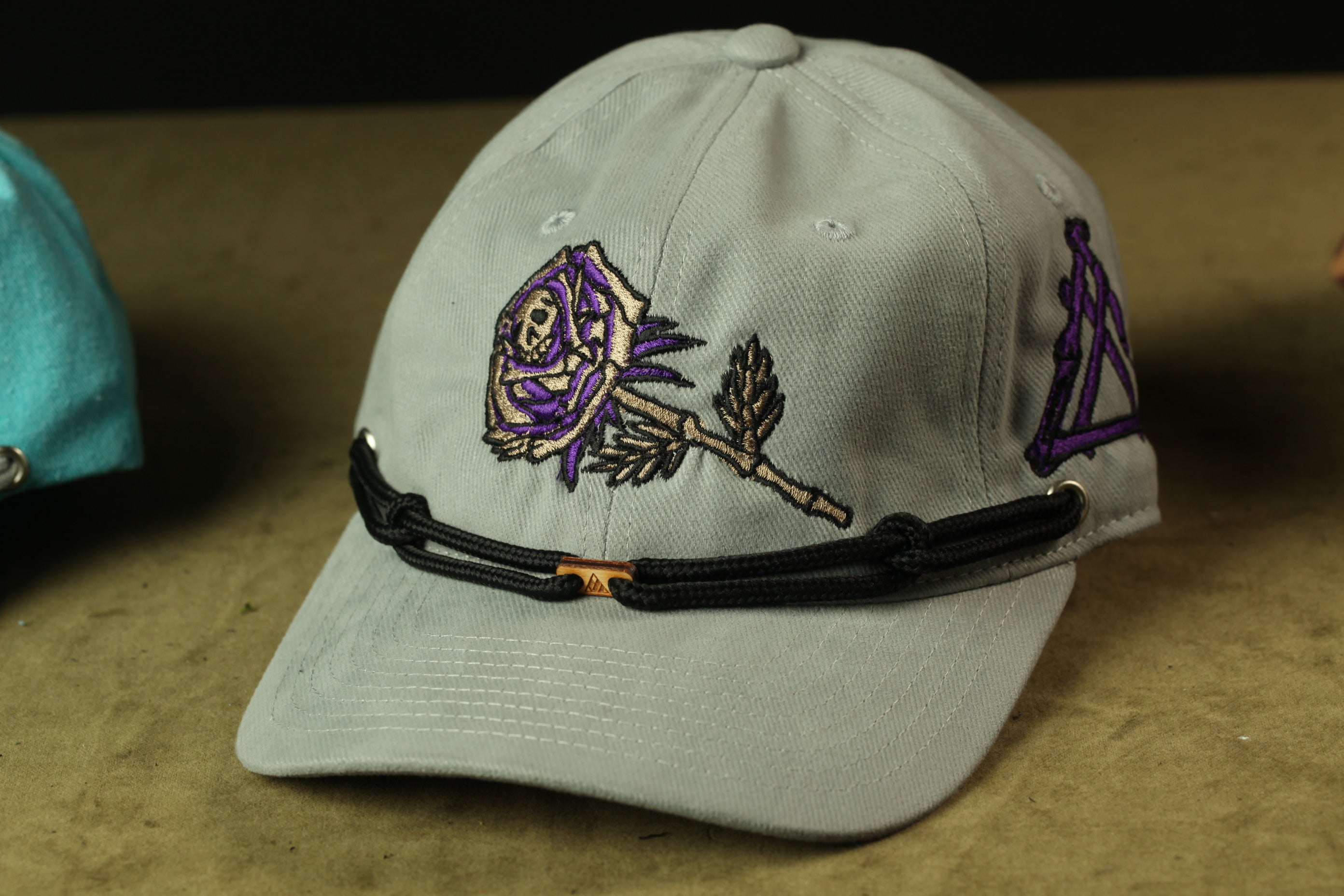 A gray baseball cap with a purple rose embroidered on it, sitting on a brown surface.