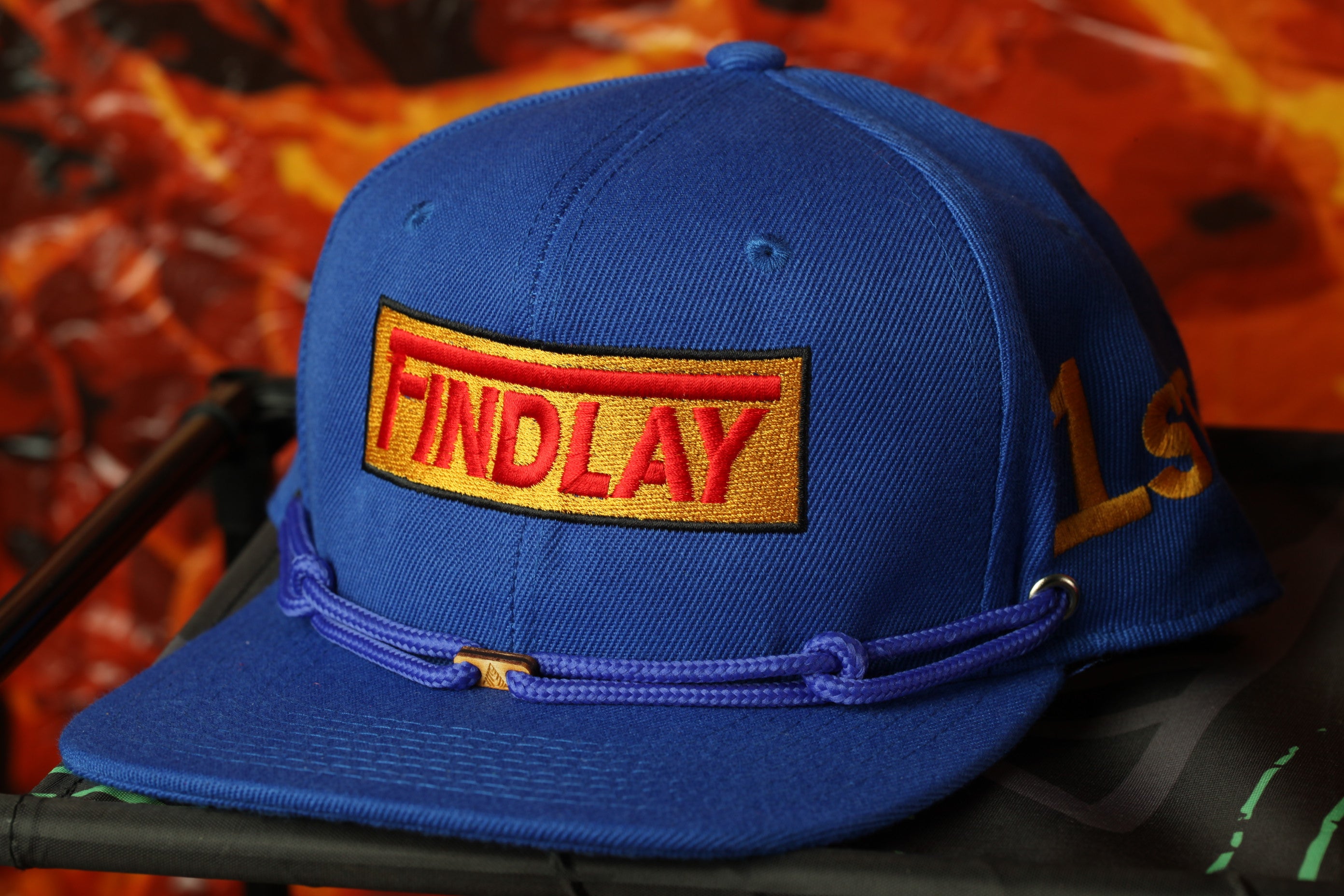 A blue baseball cap with a red and yellow logo on it, sitting on a black surface.