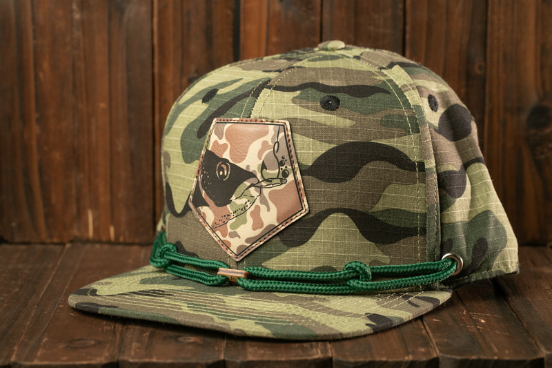 A camouflage baseball cap with a patch featuring a fish design, resting on a wooden surface.