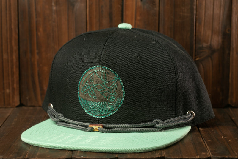A black baseball cap with a green circular logo on the front, placed on a wooden surface.