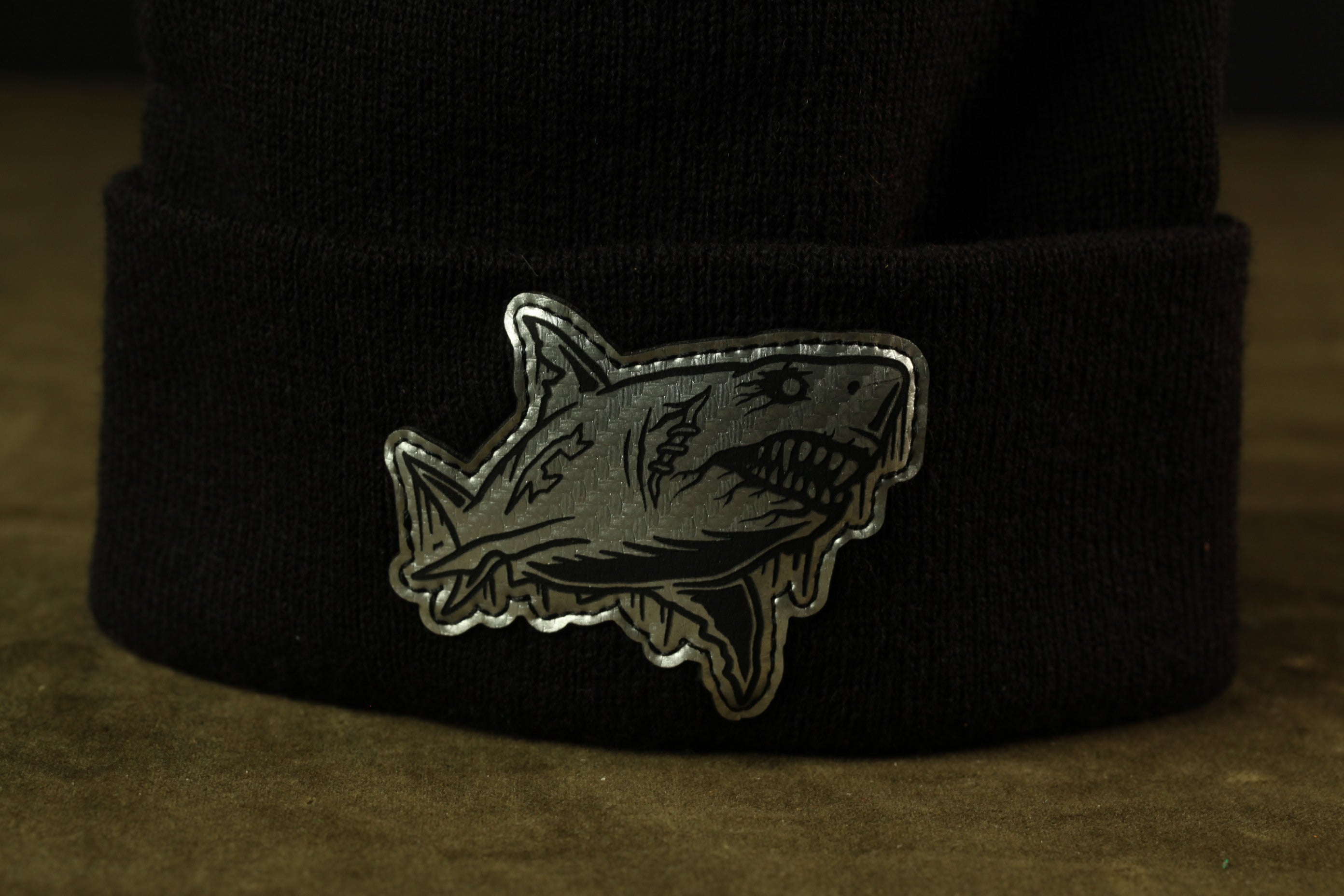 A close-up image of a black knit cap with a silver shark sticker on it.