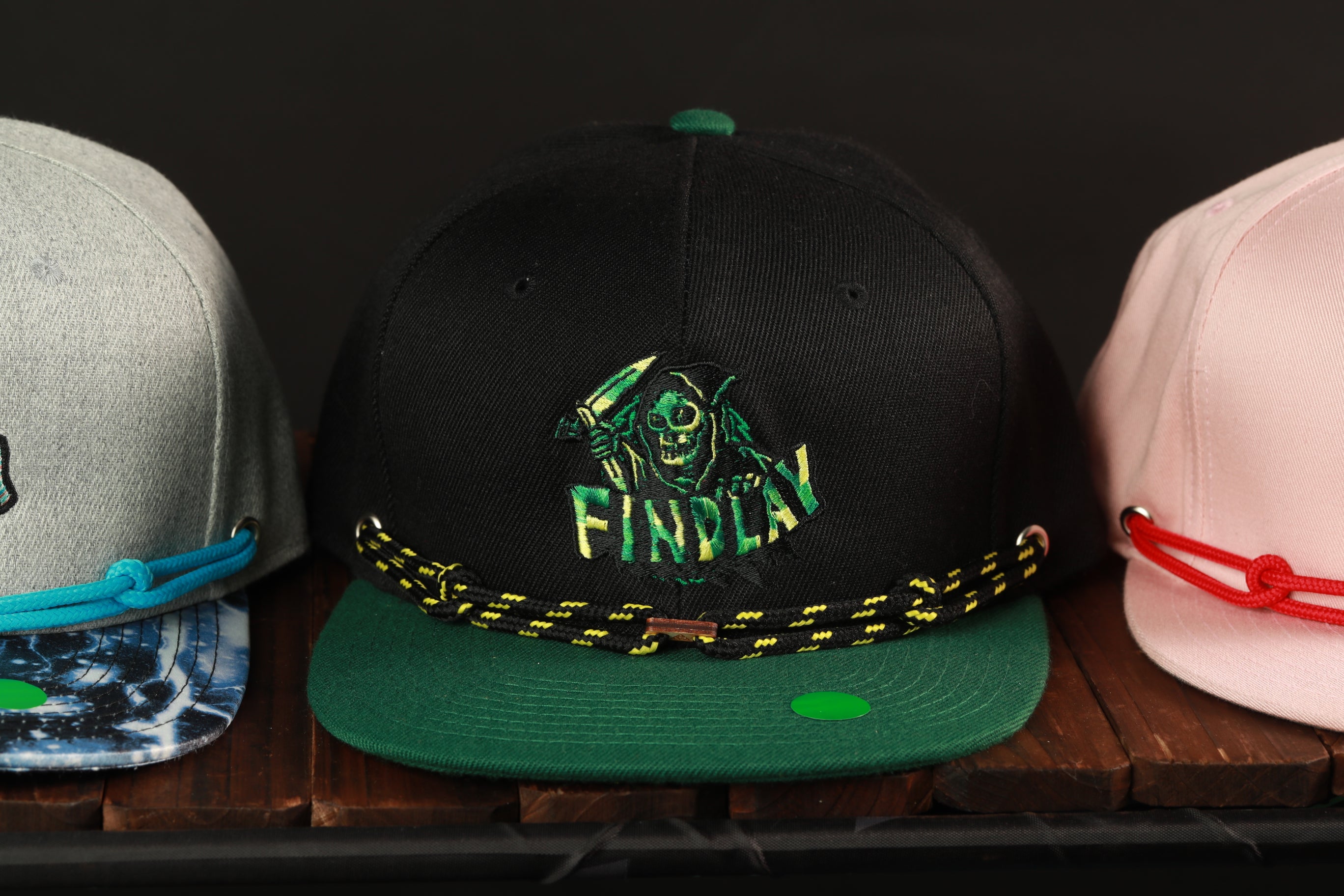 A collection of three baseball caps on a wooden surface, with the middle cap featuring a graphic design and the other two caps in different colors.