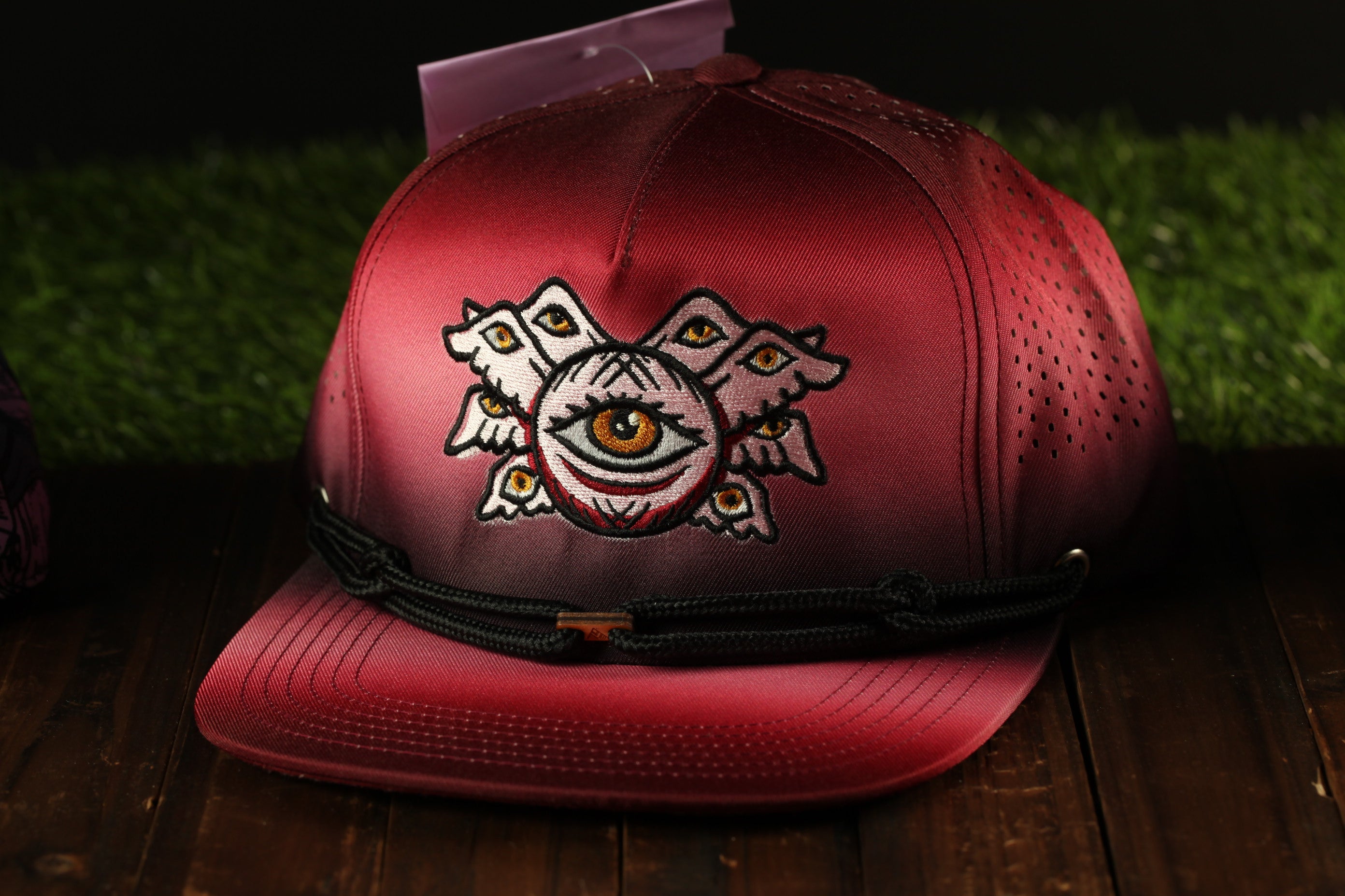 A red baseball cap with an eye design on the front, sitting on a wooden surface.