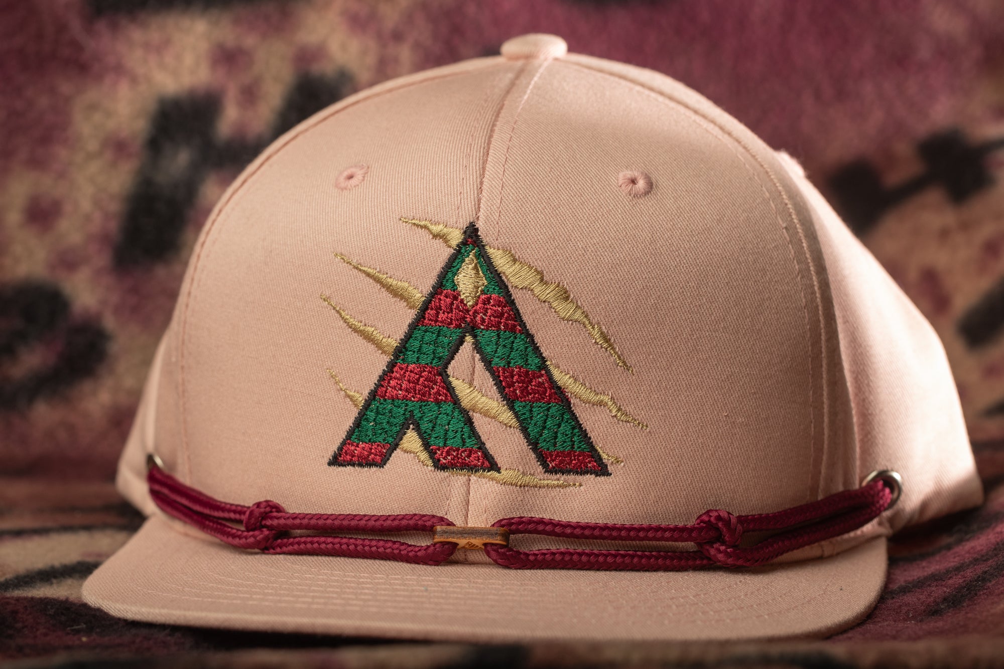 A pink baseball cap with a red and green embroidered logo on the front.