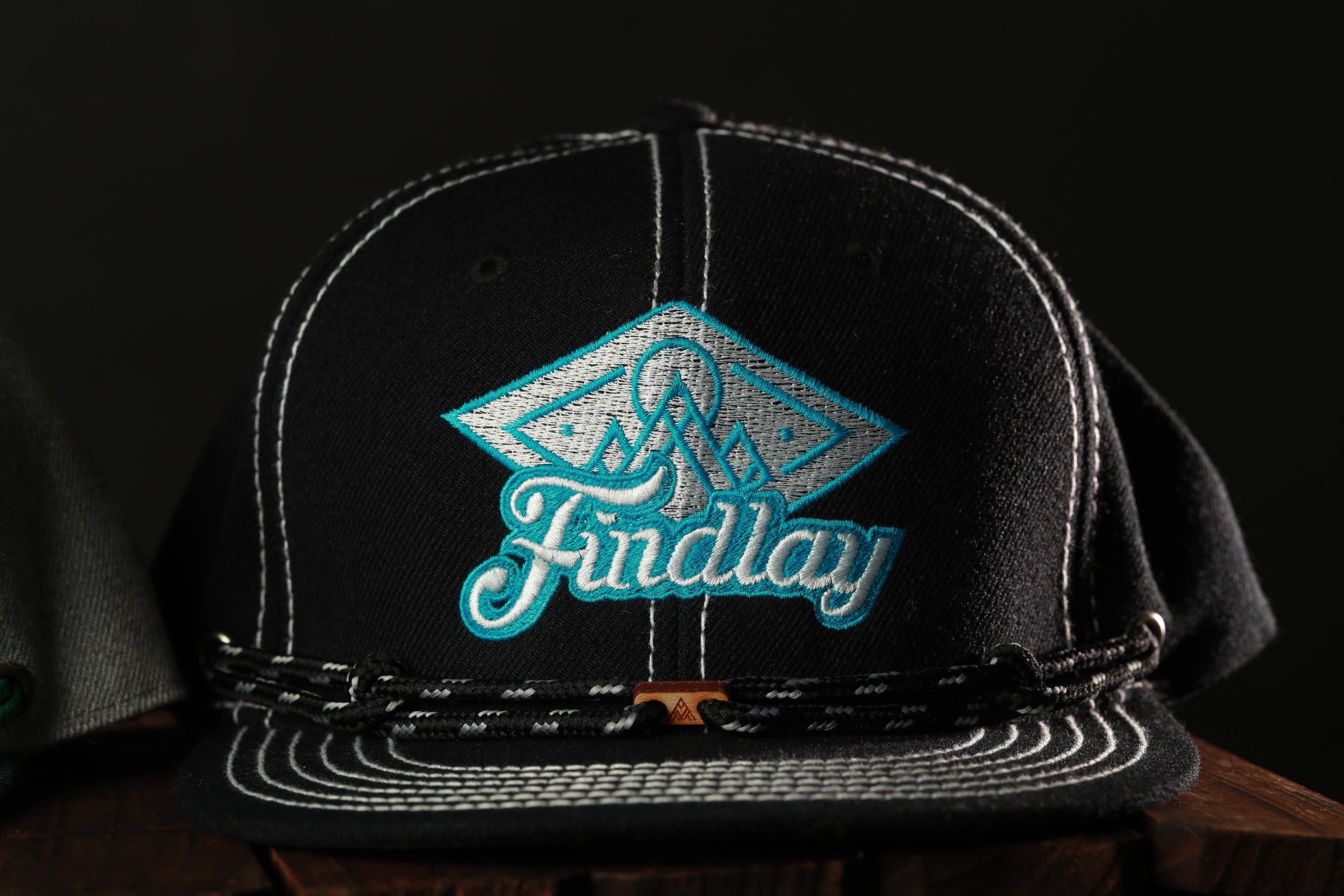 A black baseball cap with a teal logo and a black strap.
