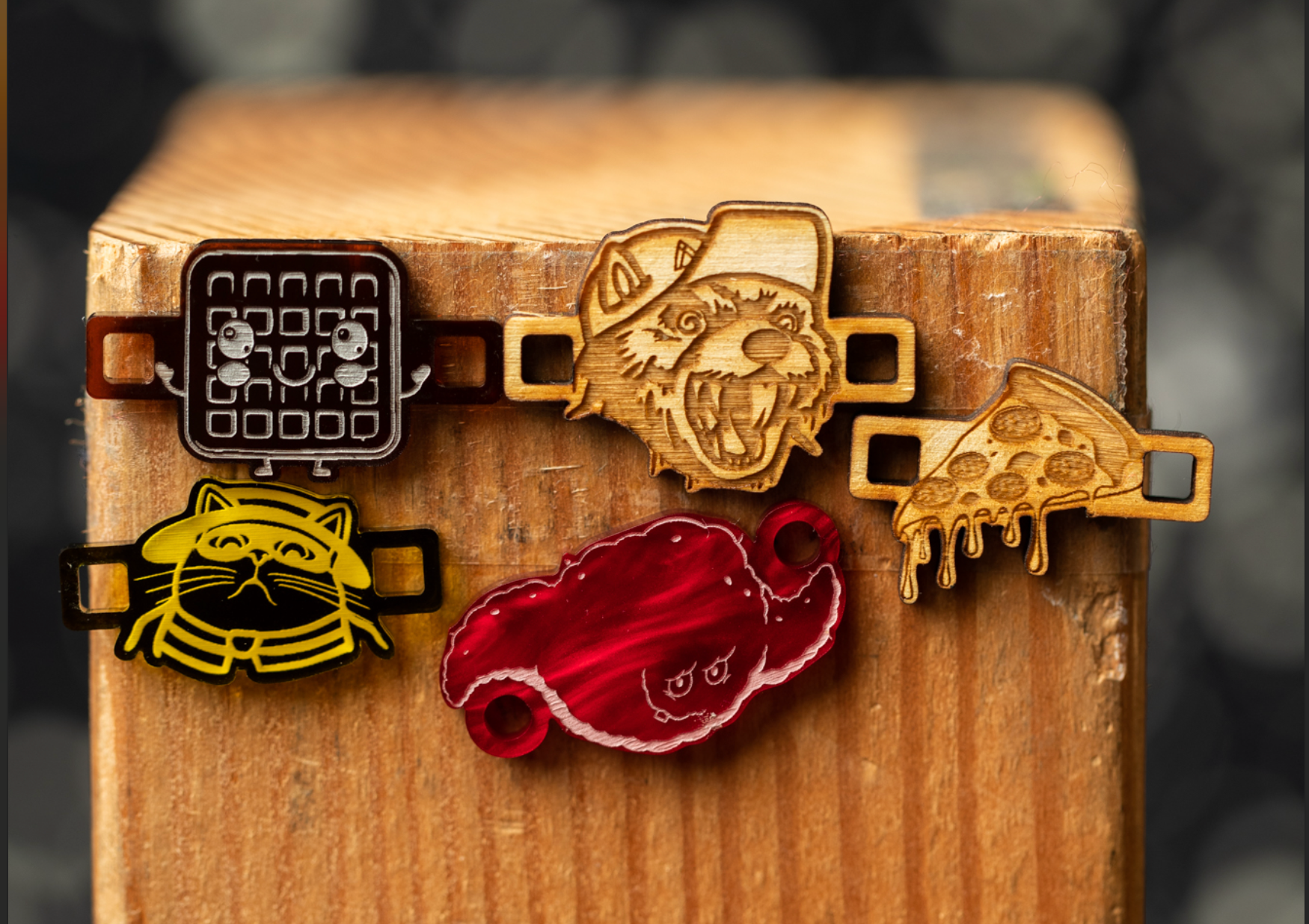 a collection of five wooden objects, including a cat, a waffle, a wolf, a slice of pizza, and a red object, all attached to a wooden surface.