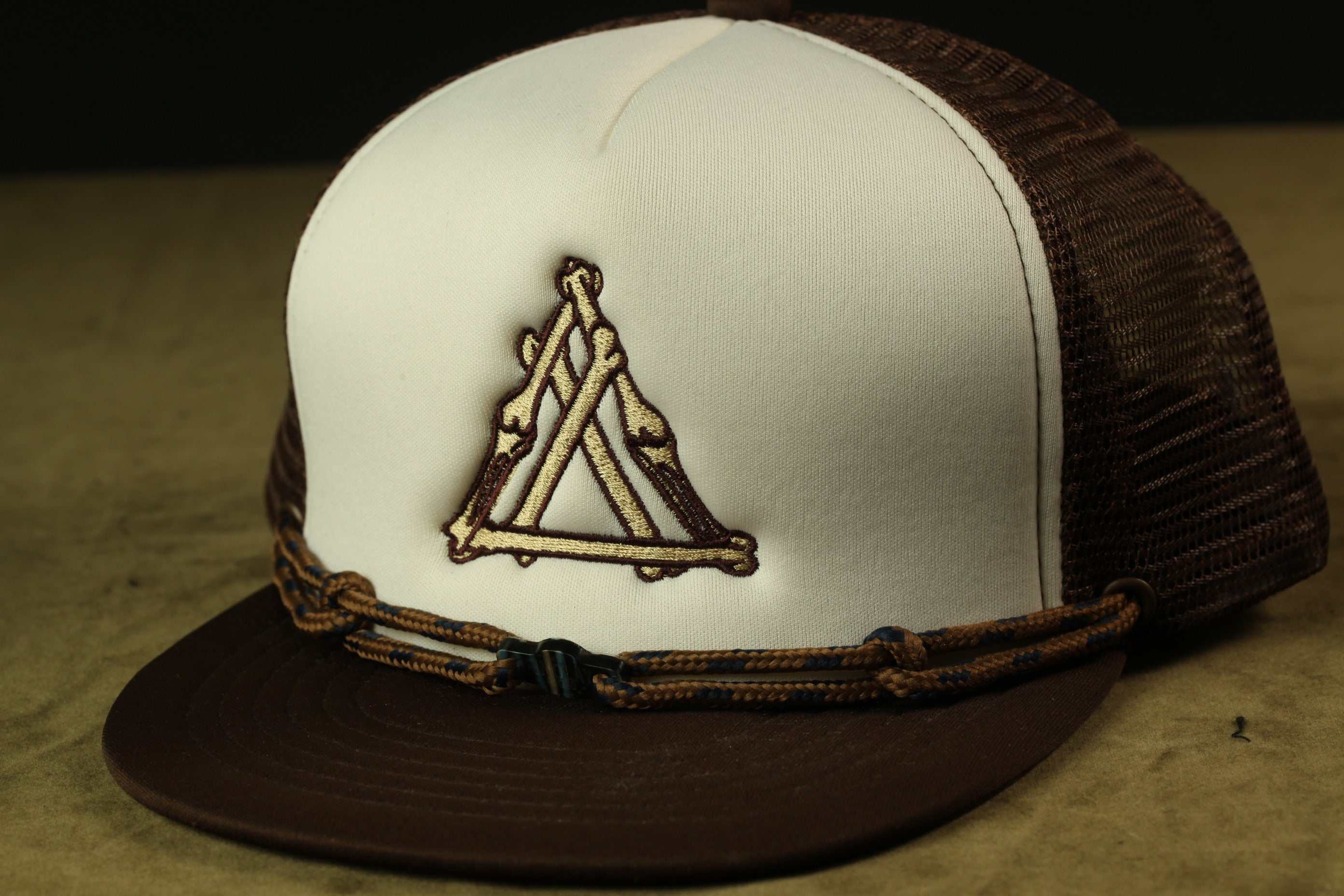 A white baseball cap with a brown band and a triangular embroidered logo on the front.