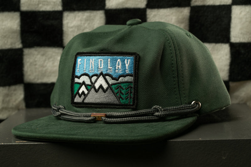 A green baseball cap with a patch on the front, featuring a mountain landscape and the word "FINDLAY" printed on it.