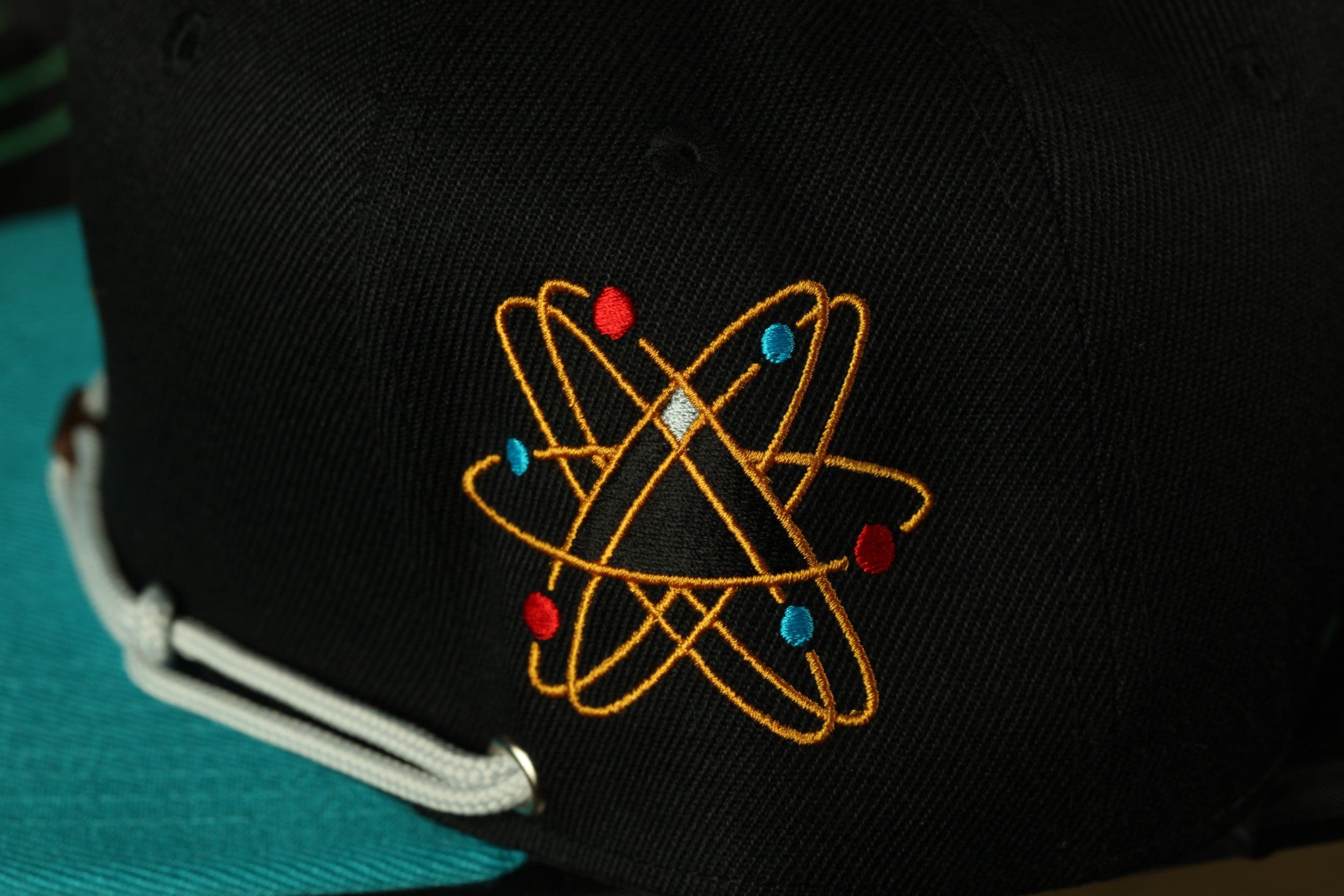 A close-up view of a black baseball cap with a colorful, intricate embroidered design on the front.