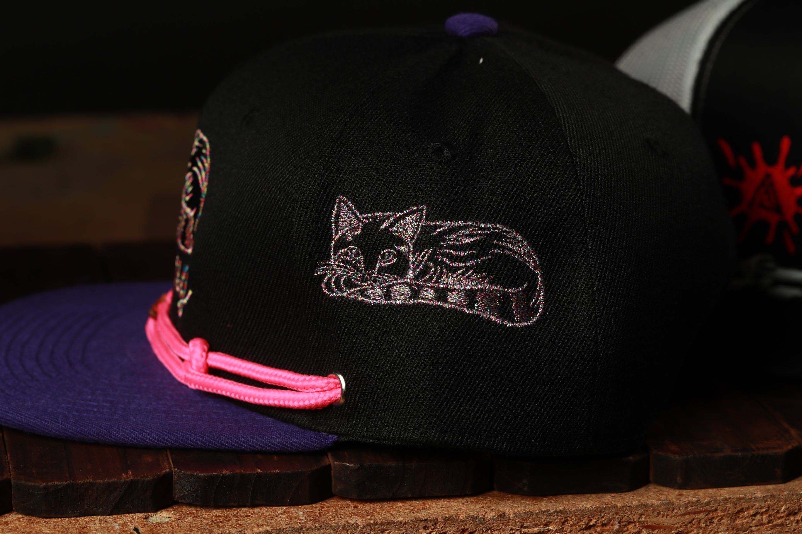 A close-up view of a black baseball cap with a cat embroidered on it, resting on a wooden surface.