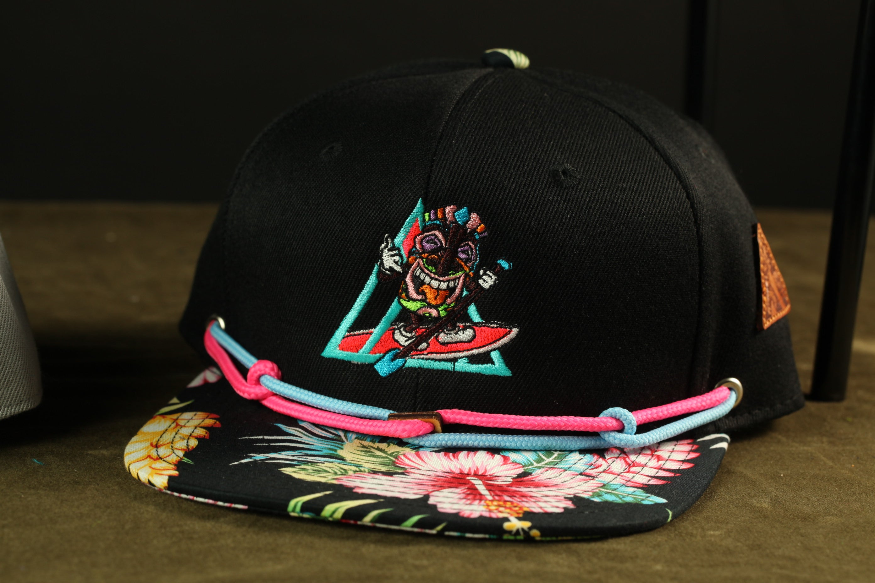 A black baseball cap with a colorful, cartoonish design featuring a character riding a skateboard.