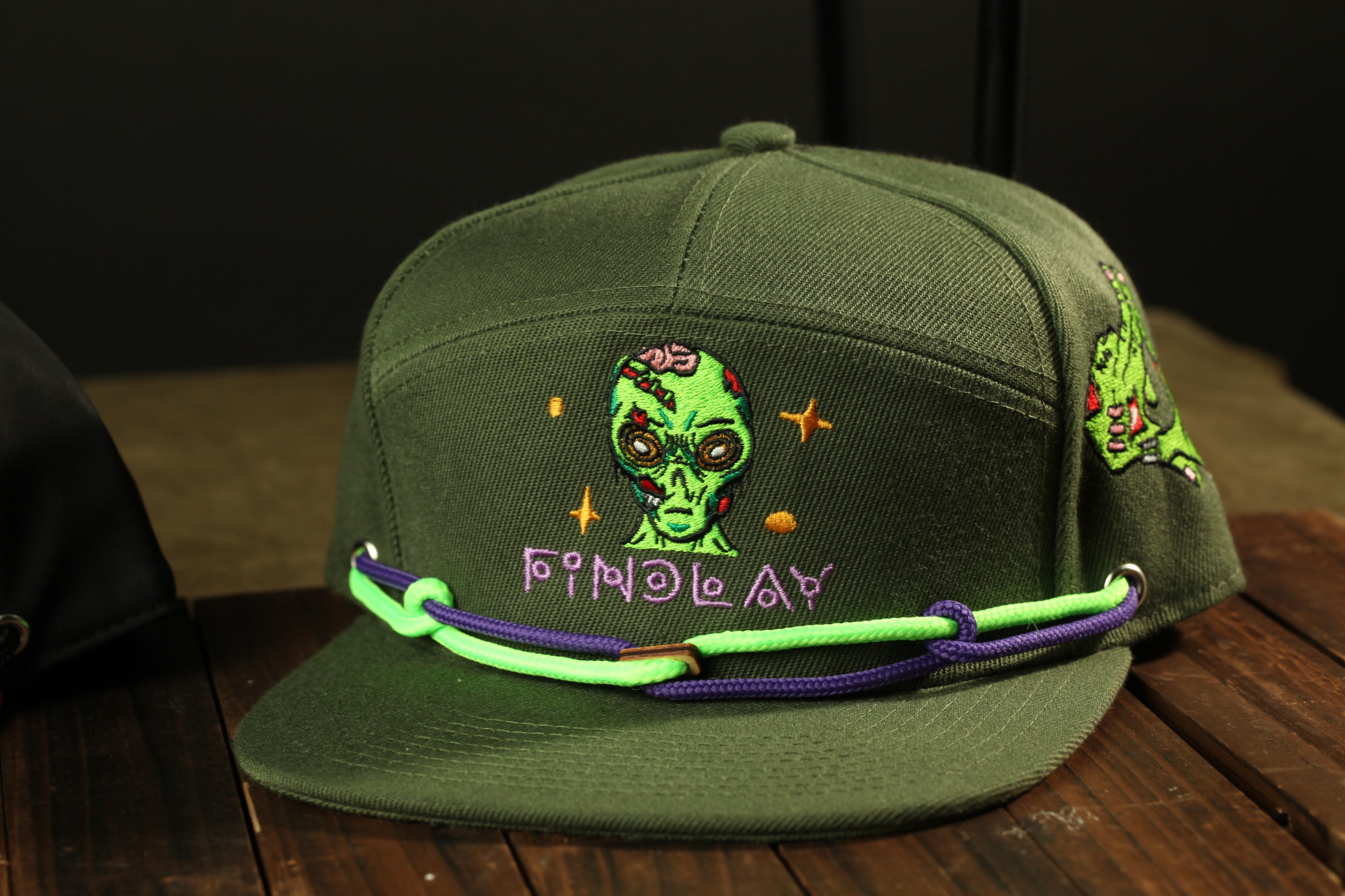 A green baseball cap with a graphic of an alien face and the word "Fozzie" on it, along with a purple and green chain strap.