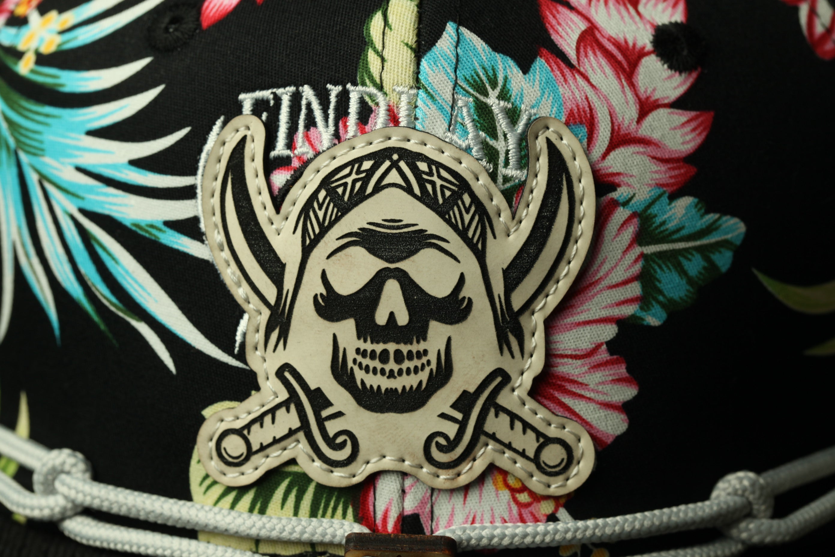 A close-up of a black and white pirate-themed patch on a black background with colorful tropical flowers.