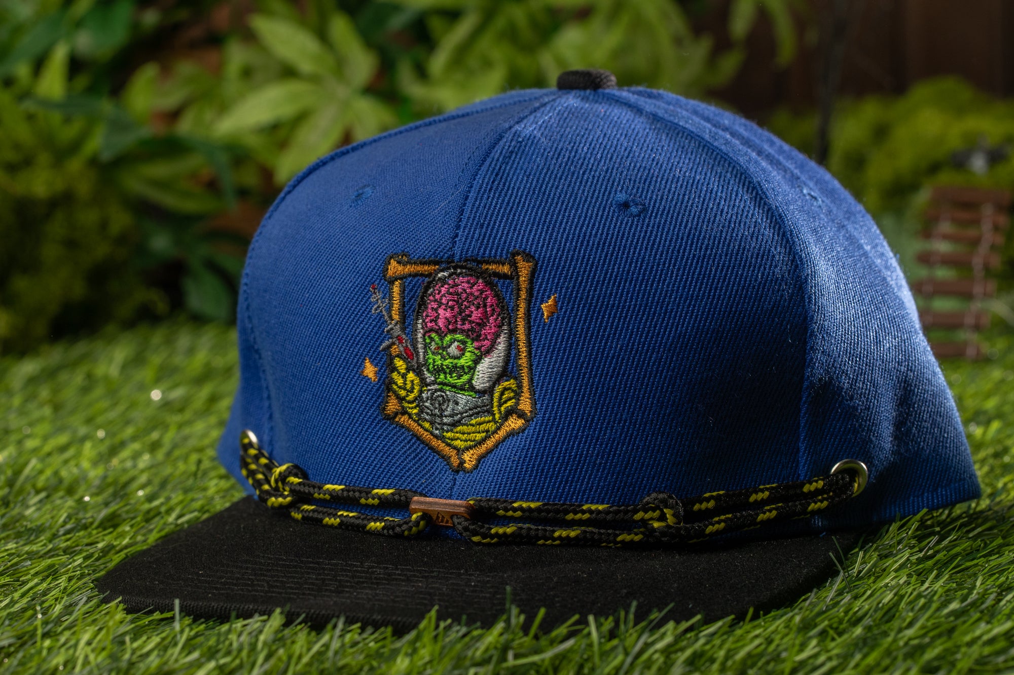 A blue baseball cap with a colorful embroidered design on the front, placed on a grassy surface.