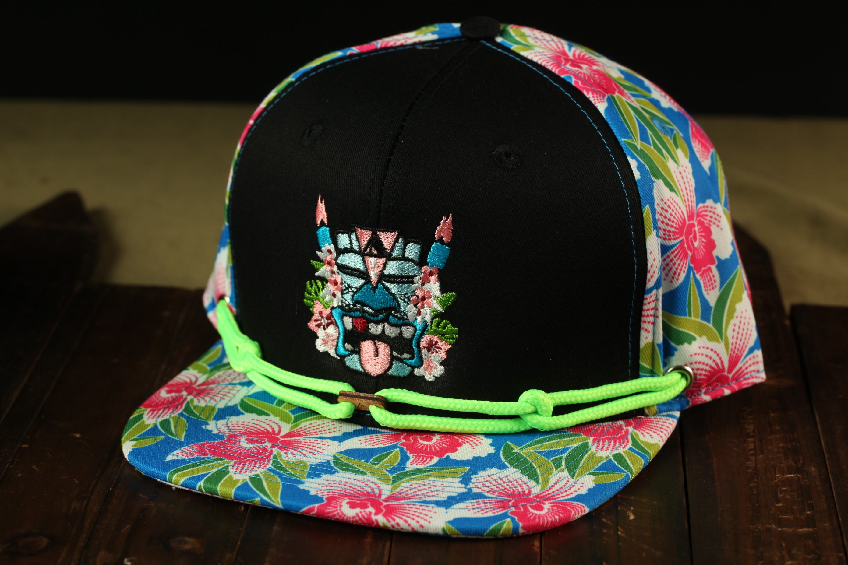 A colorful floral-patterned baseball cap with a black brim and a graphic design on the front, sitting on a wooden surface.