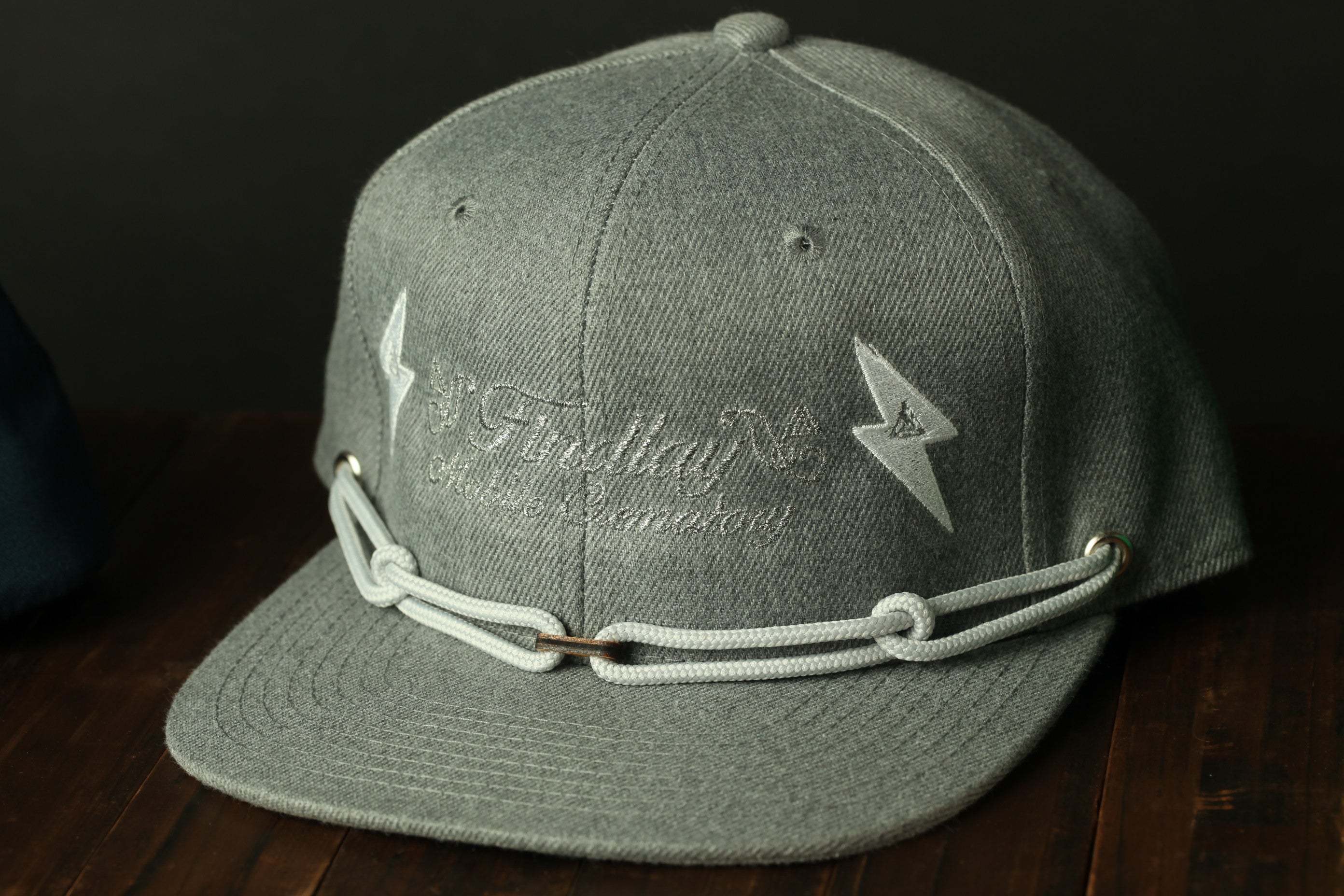 A gray baseball cap with a chain strap and white lightning bolt designs on the front.