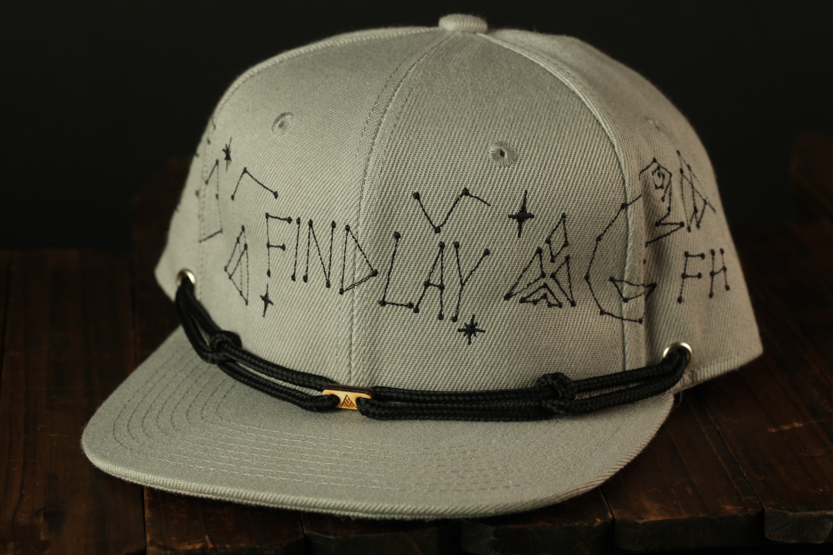 A gray baseball cap with a black strap and embroidered text on the front.