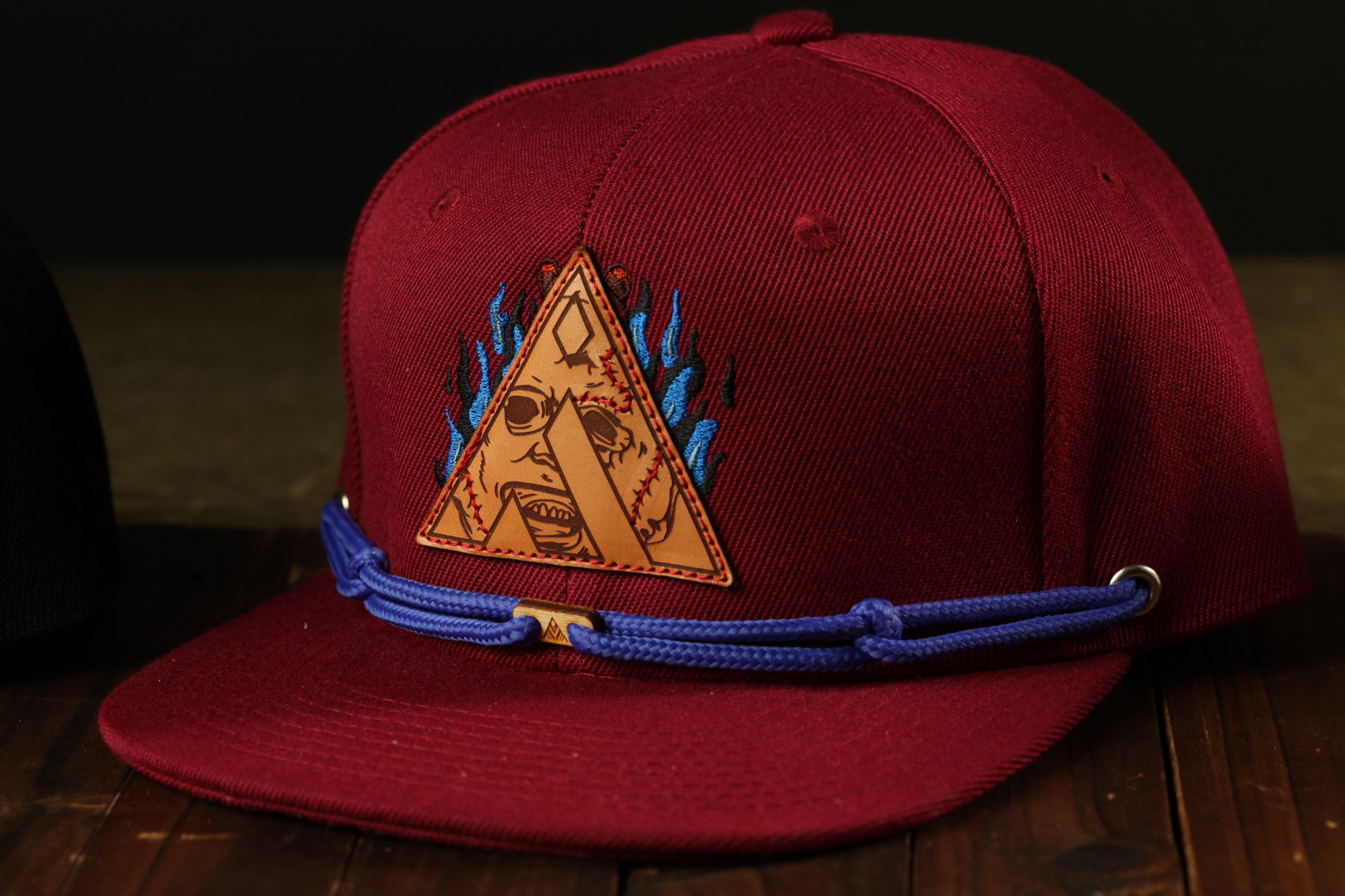 A maroon baseball cap with a blue and orange triangle-shaped logo on the front, sitting on a wooden surface.