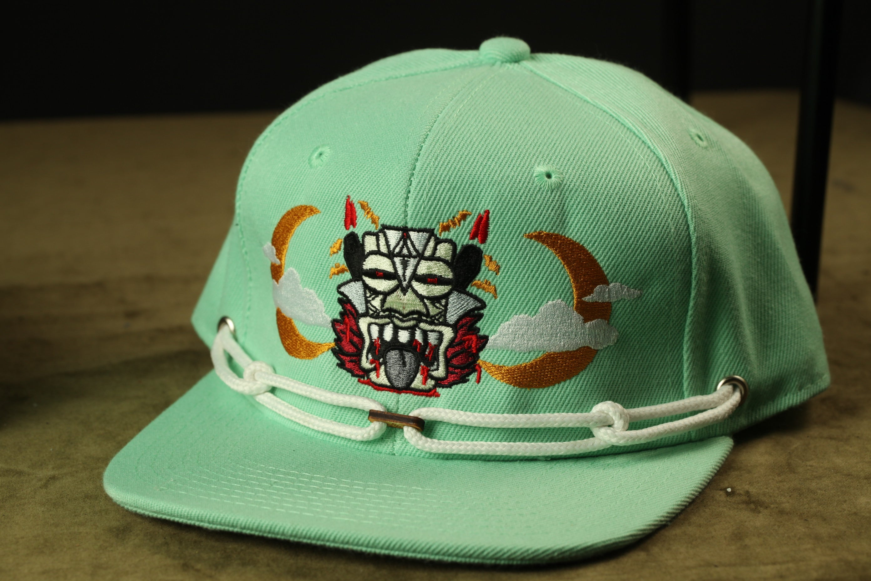 A mint green baseball cap with a unique design featuring a skull and crescent moon on the front.