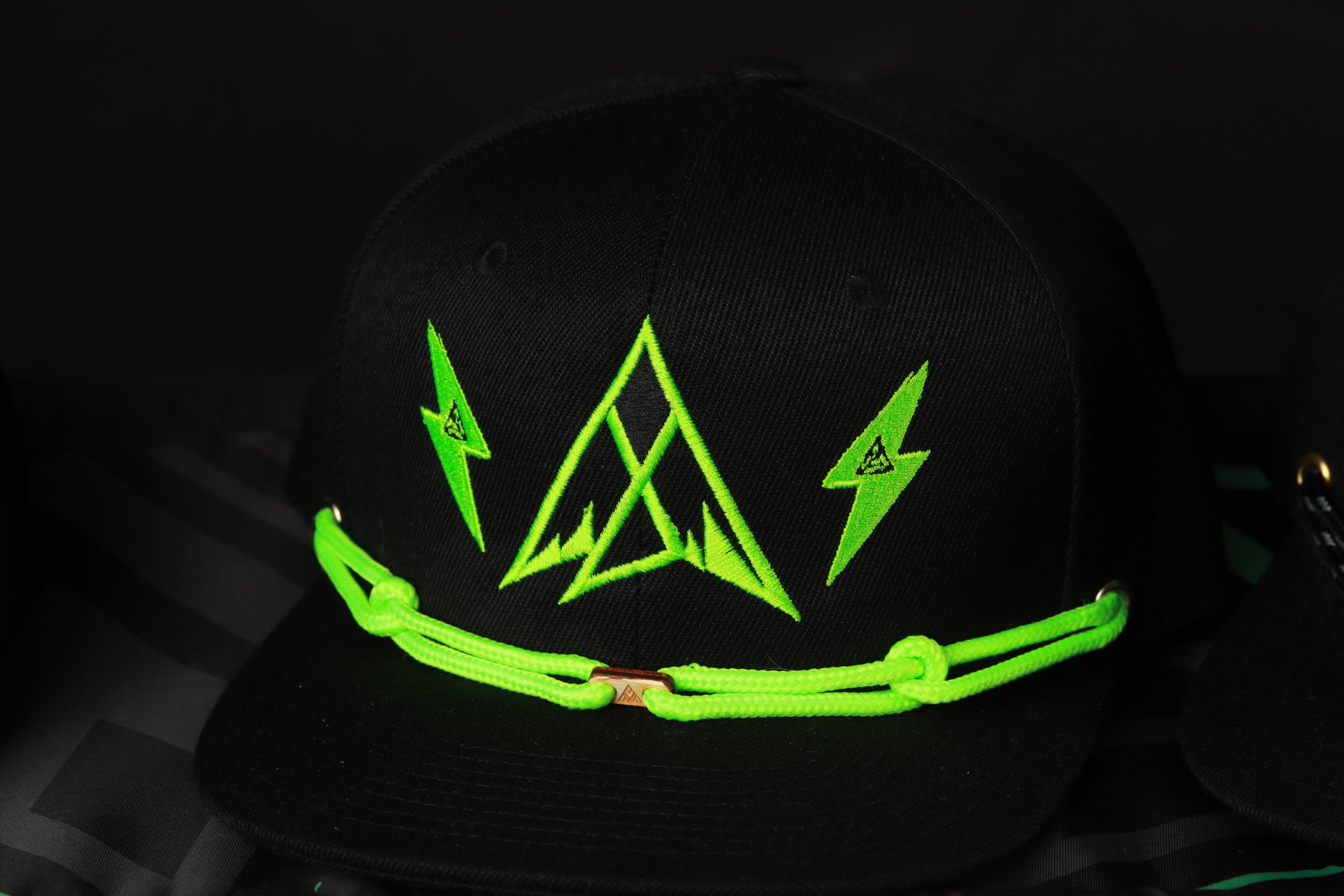 A black baseball cap with a neon green lightning bolt design and a triangle pattern on the front.