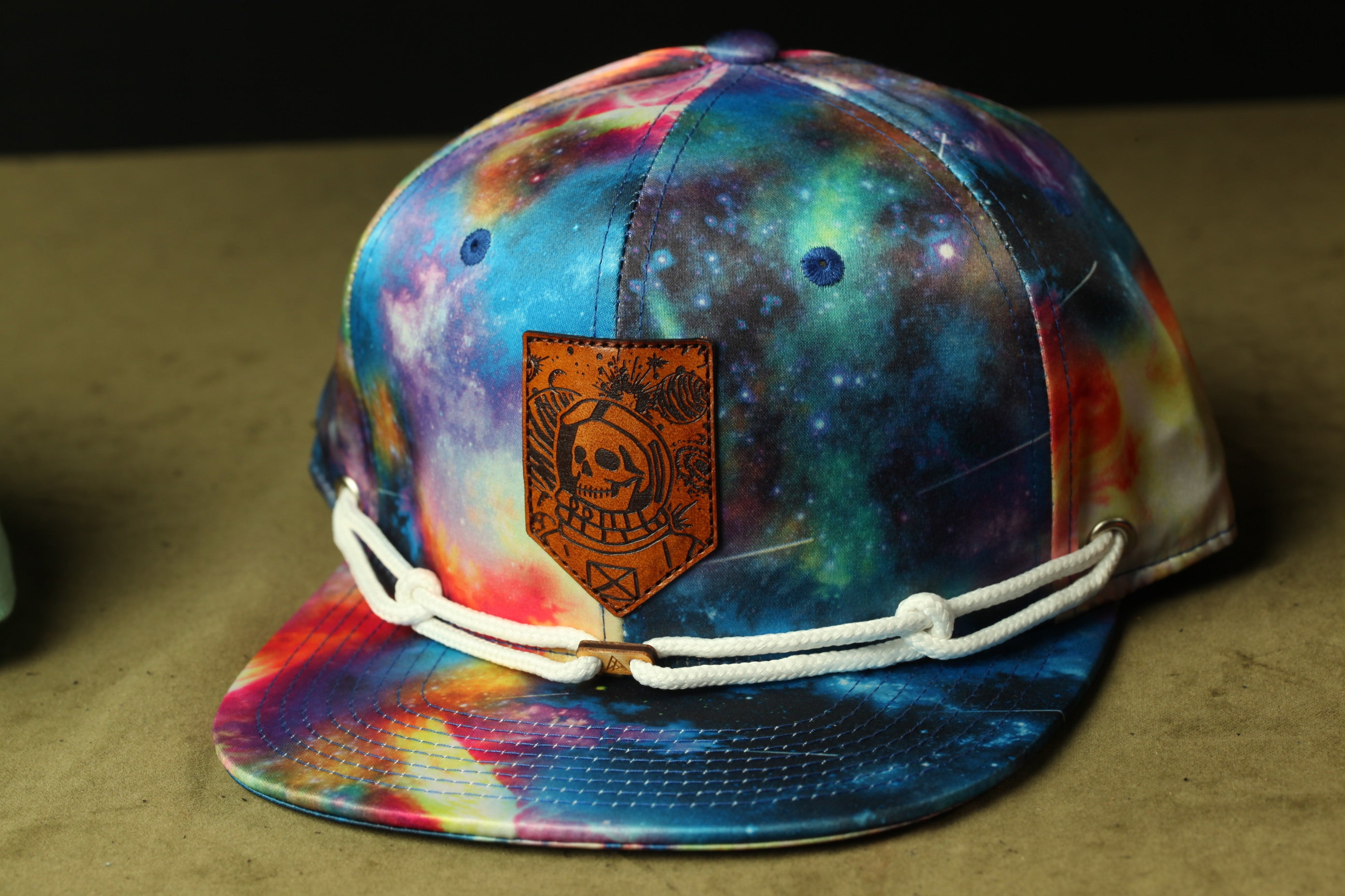 A colorful, tie-dye baseball cap with a skull and crossbones design on the front, featuring a leather patch with a similar skull and crossbones design.