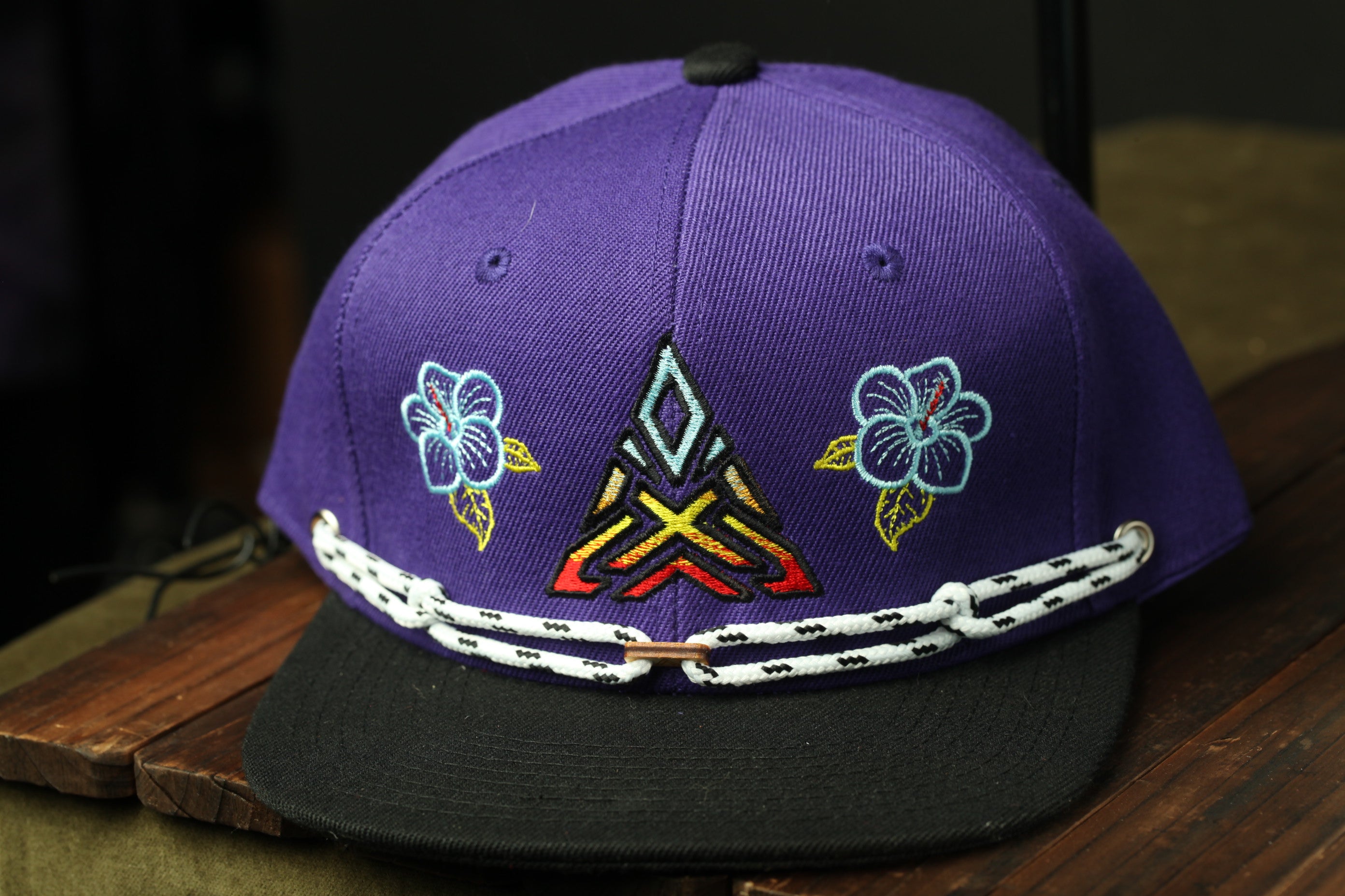 A purple baseball cap with a floral design and a geometric pattern on the front.