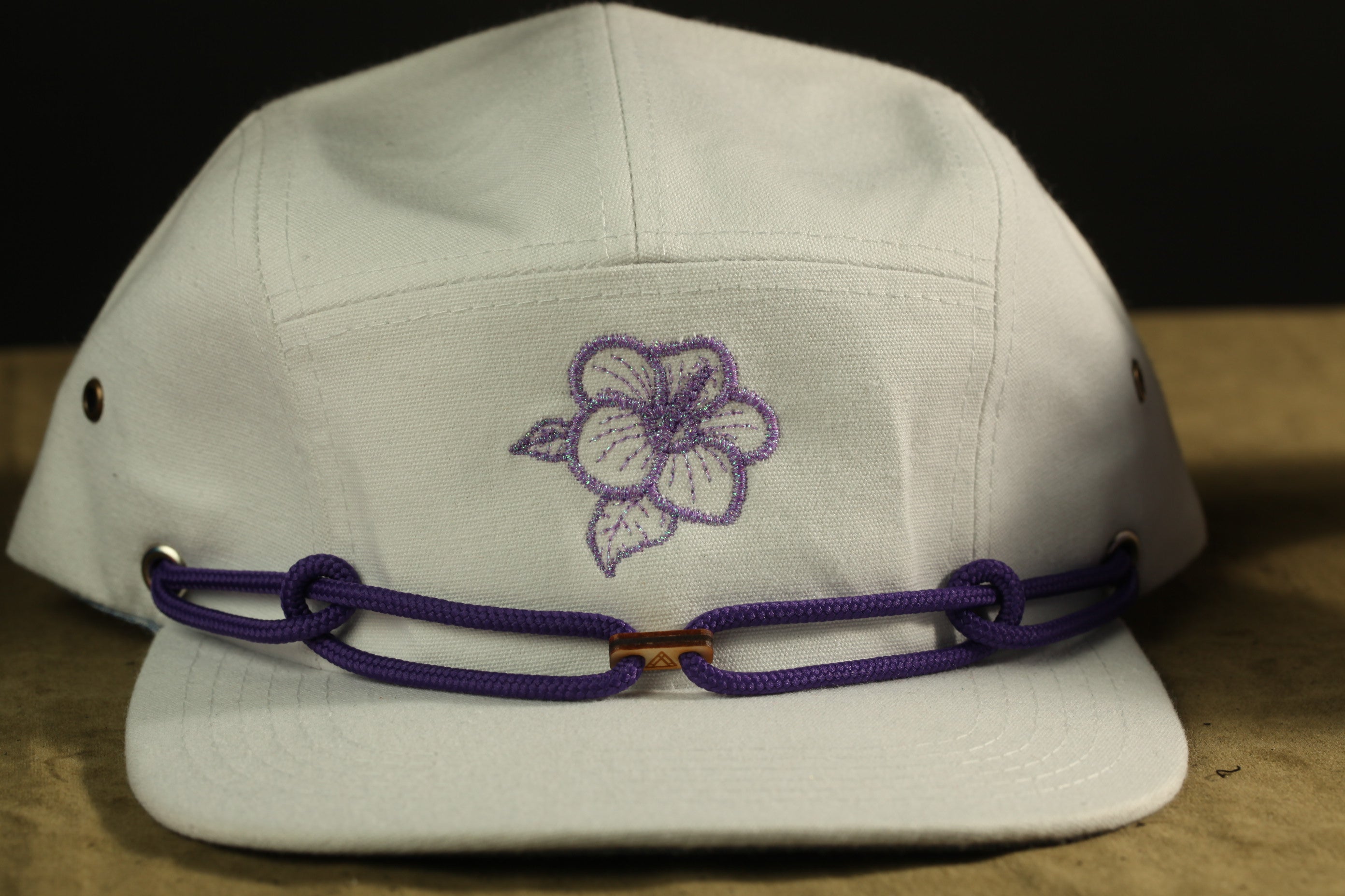 A white baseball cap with a purple flower embroidered on the front.