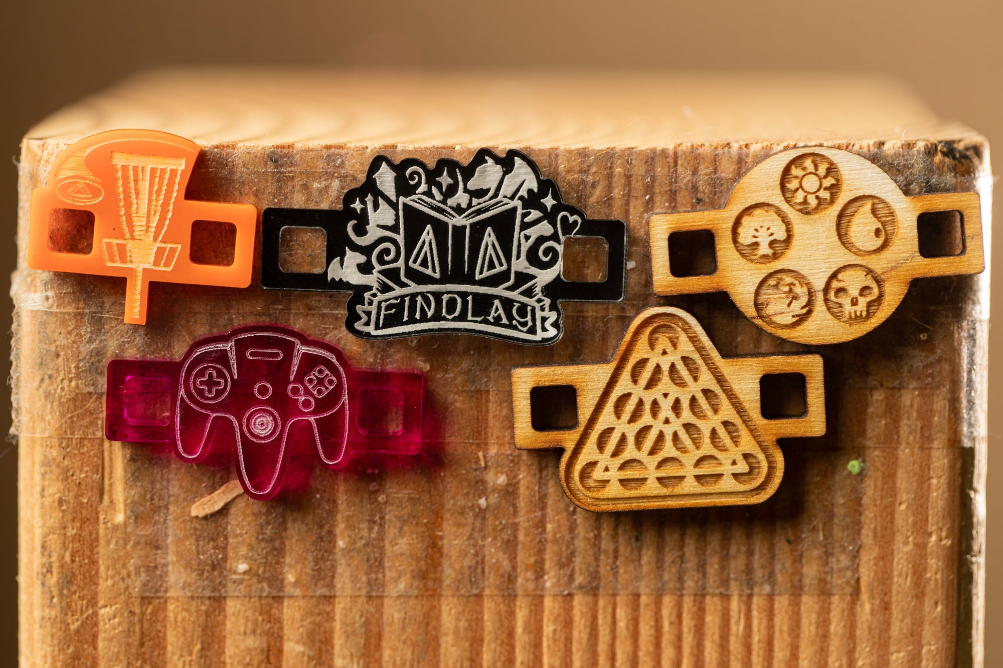 a collection of five wooden objects, including a frisbee, a video game controller, a triangular object, a skull and crossbones, and a shield with various symbols.