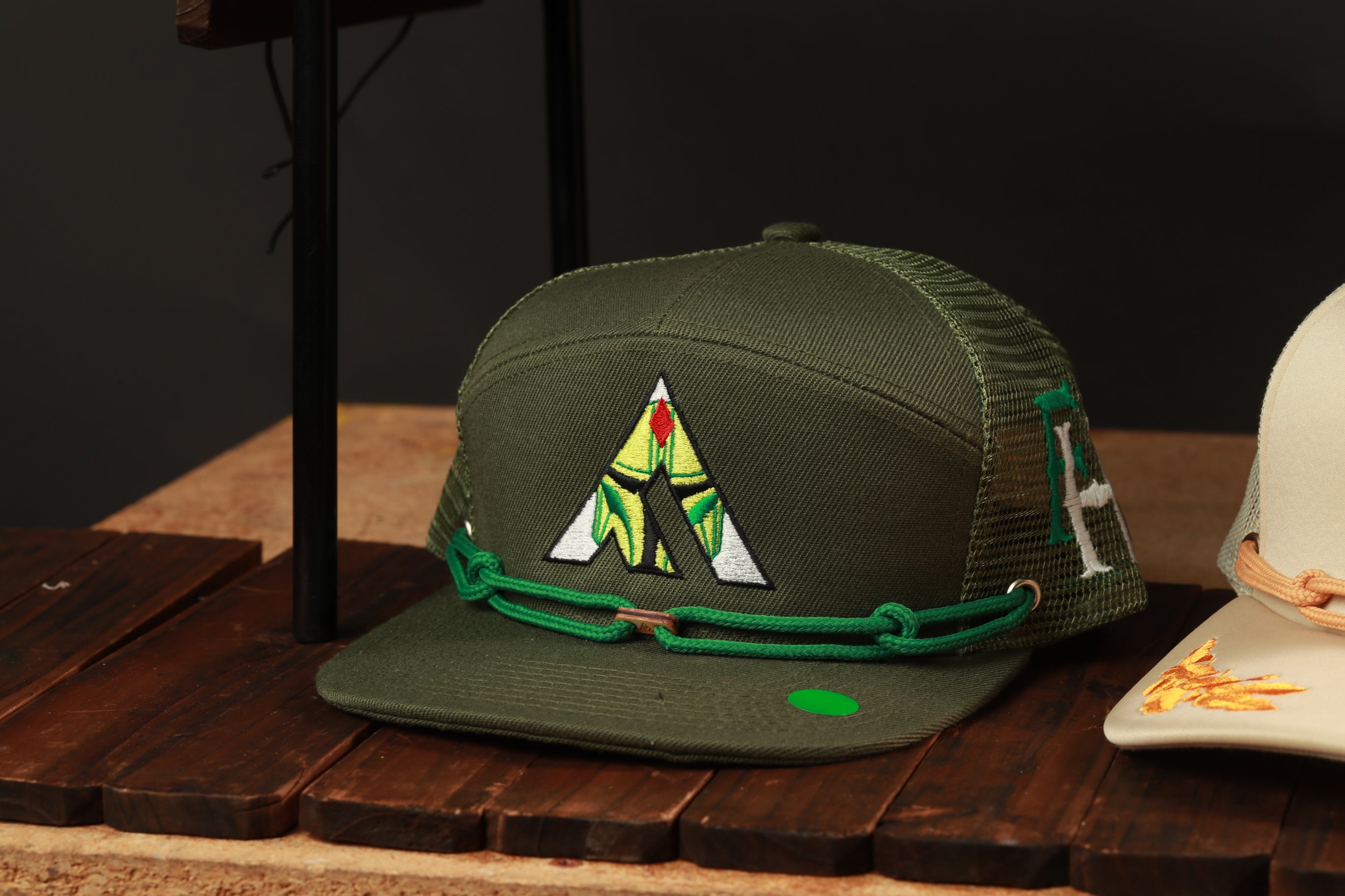 A green baseball cap with a yellow and green design on the front, sitting on a wooden surface.