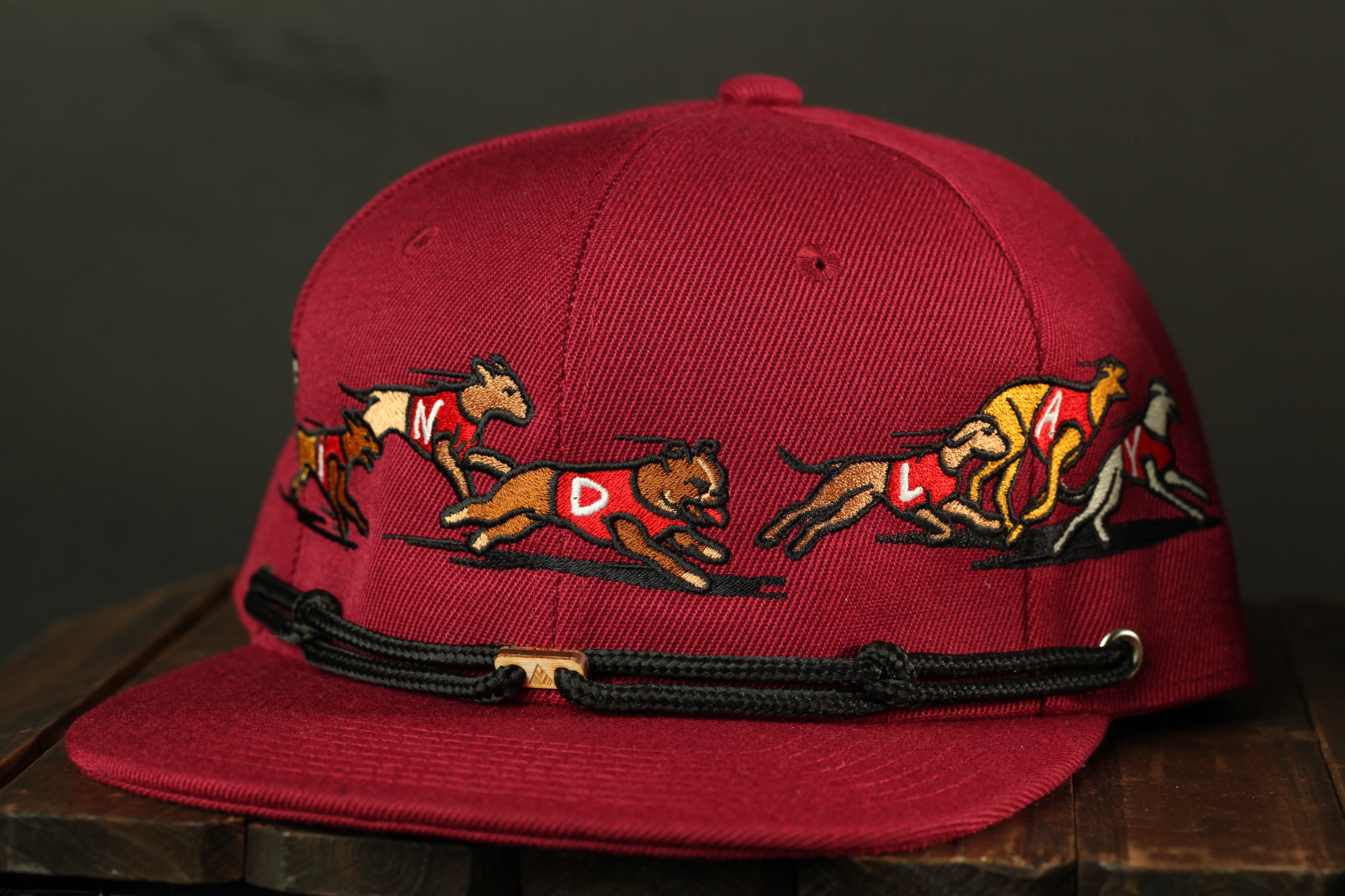 A red baseball cap with a black strap and embroidered designs of dogs running.