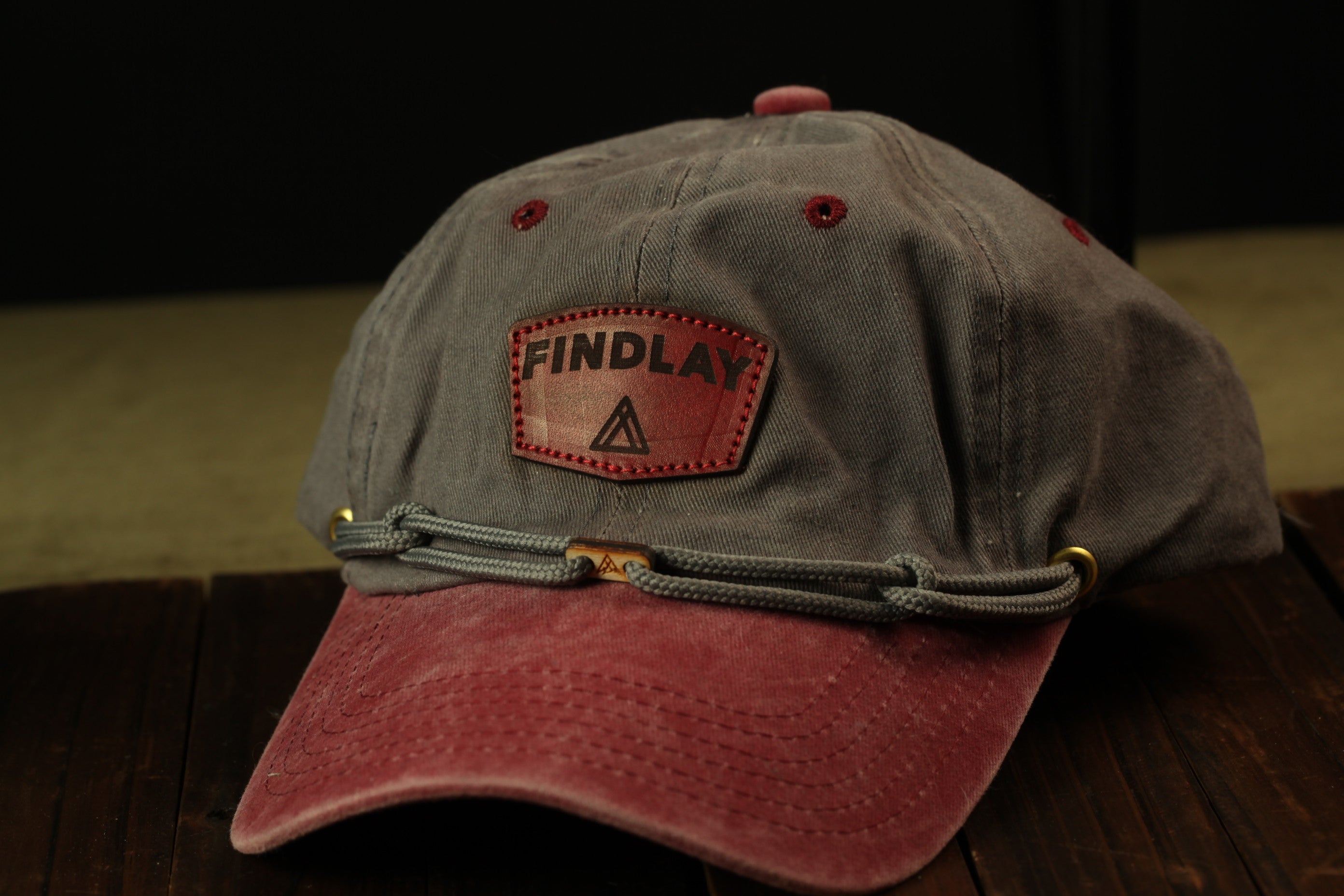 A gray baseball cap with a red brim and a red and gray patch on the front, displaying the word "FINDLAY" in black text.