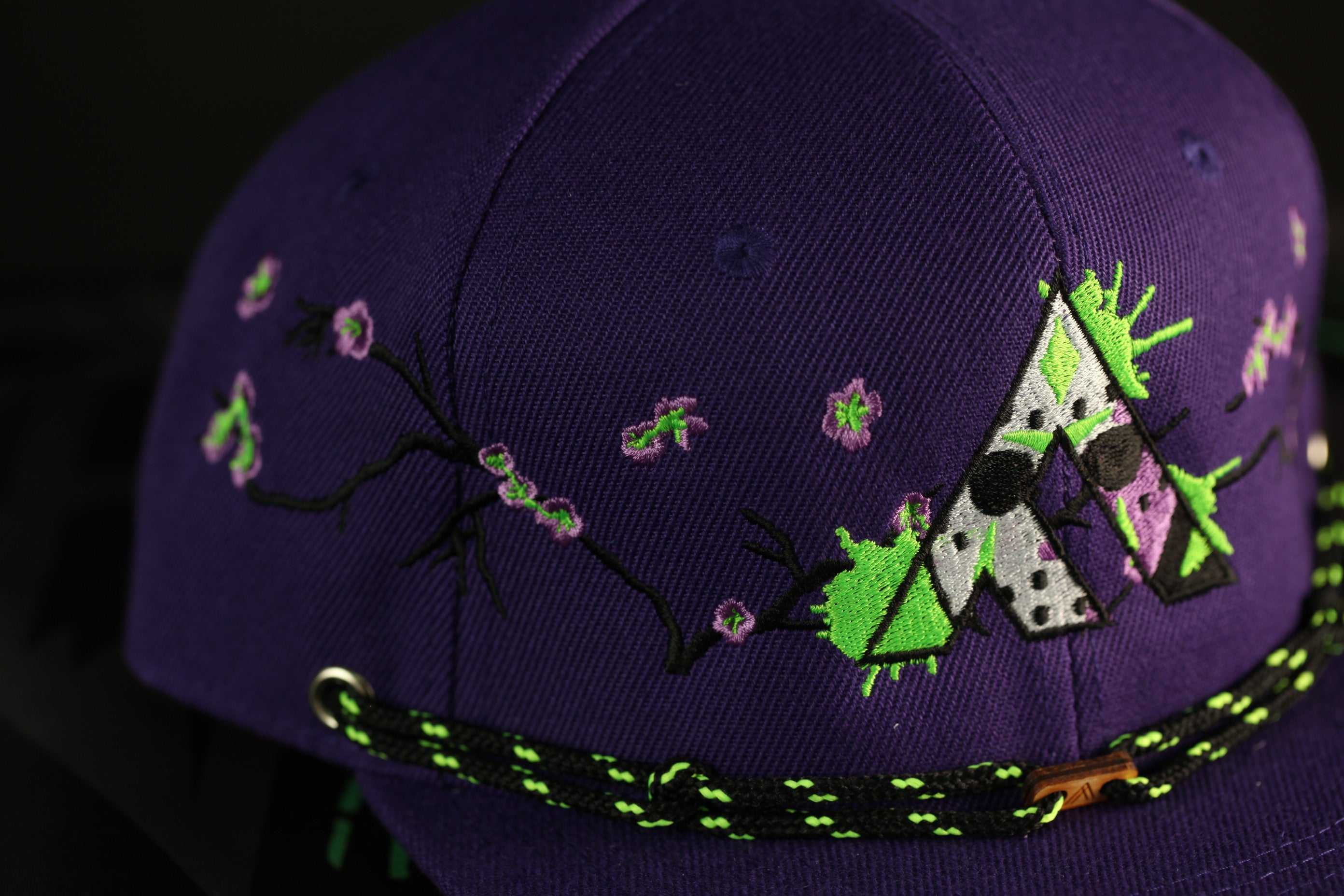 A close-up view of a purple baseball cap with a floral pattern and a green and black strap.