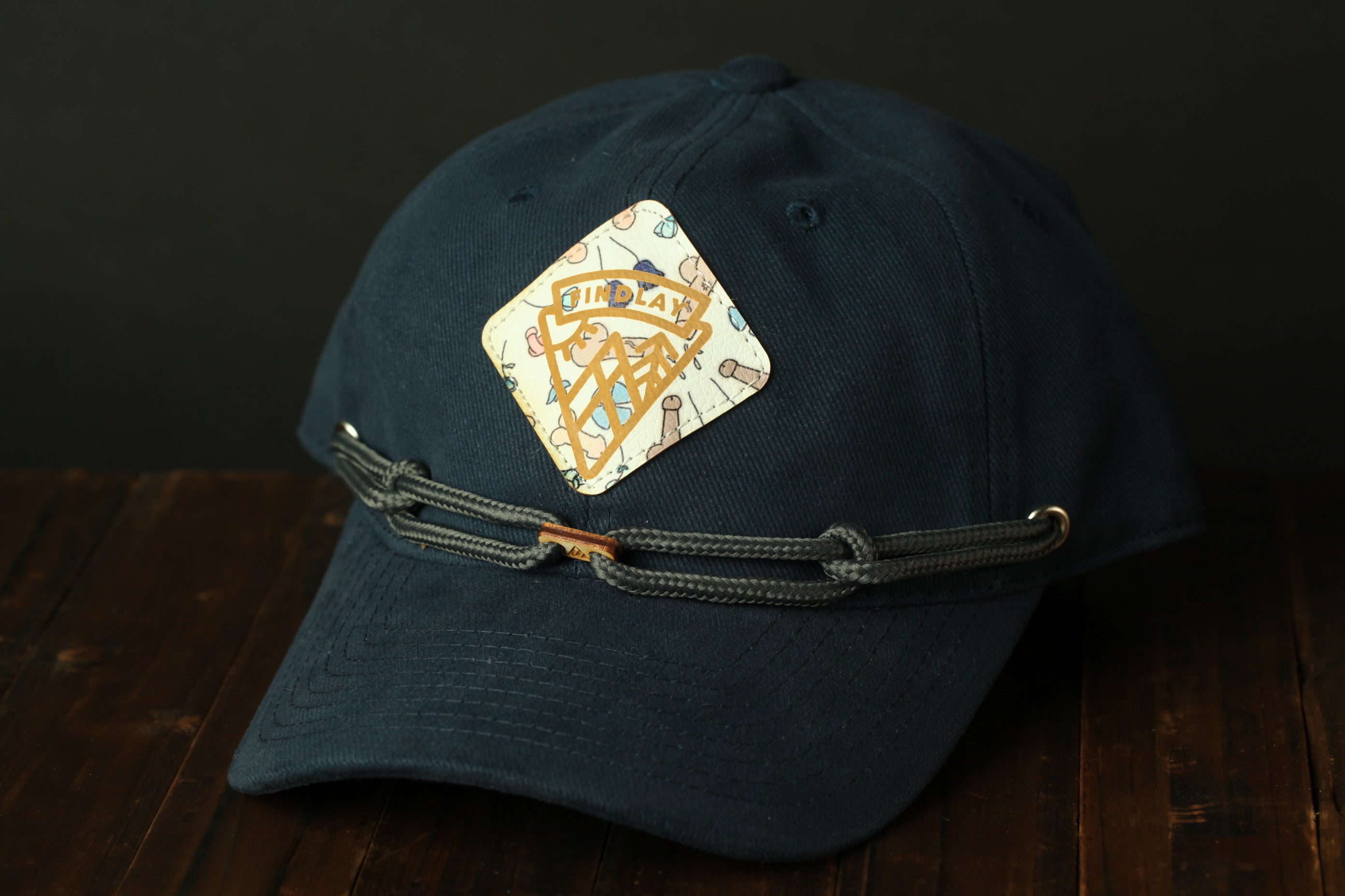 A navy blue baseball cap with a decorative patch on the front, sitting on a wooden surface.
