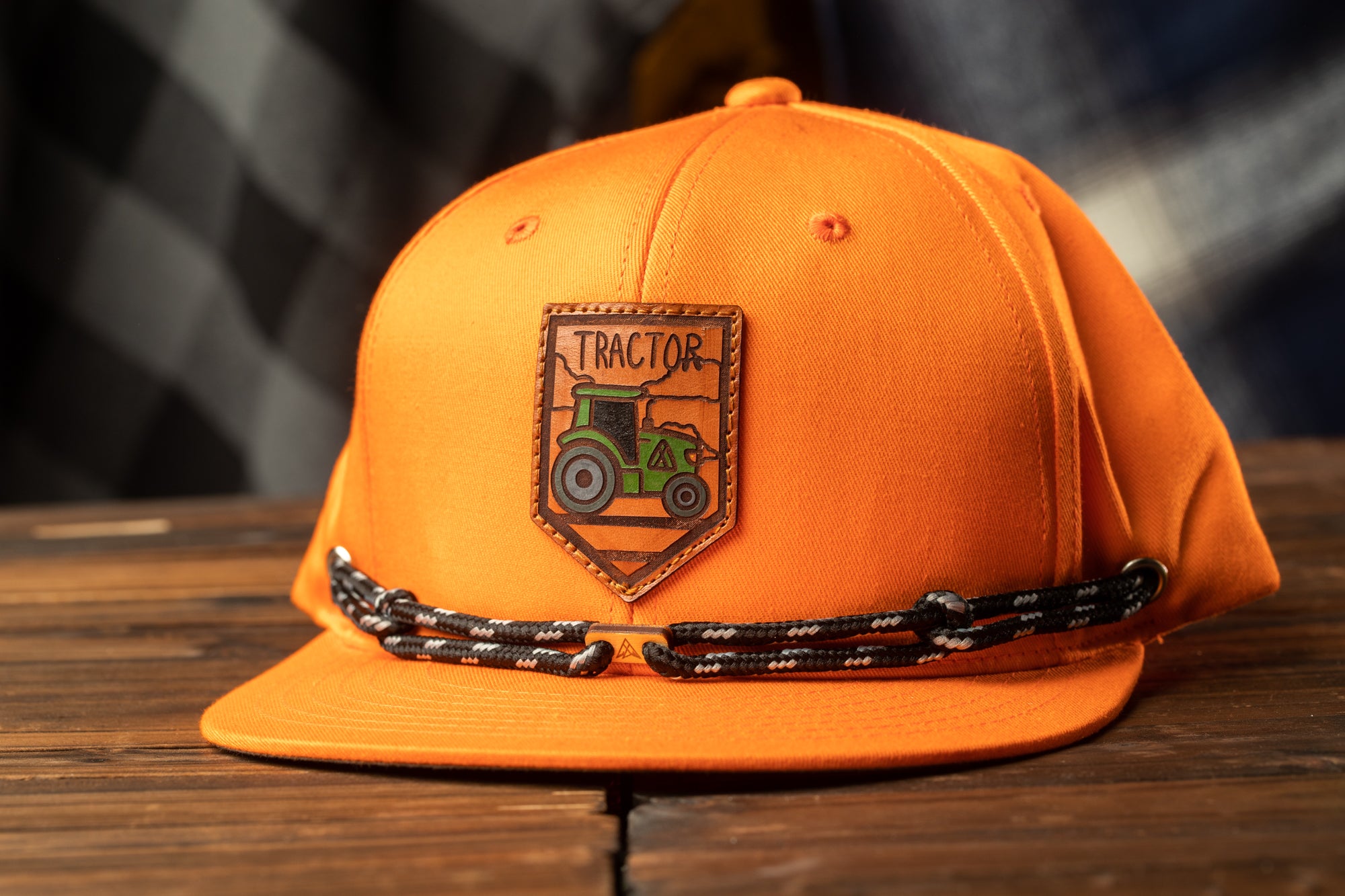 An orange baseball cap with a tractor logo on it, placed on a wooden surface.