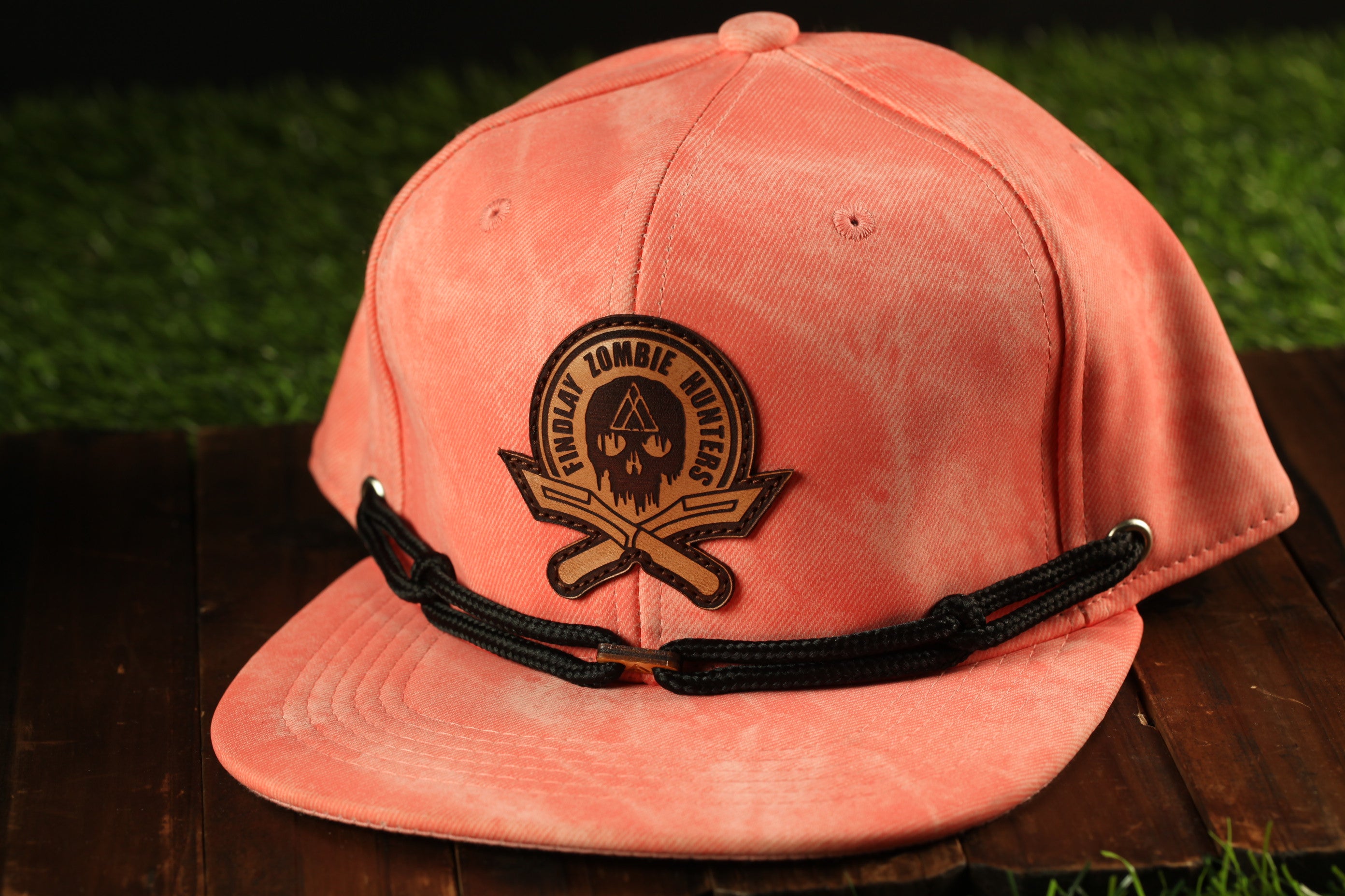 A pink baseball cap with a black strap and a circular logo on the front, placed on a wooden surface.
