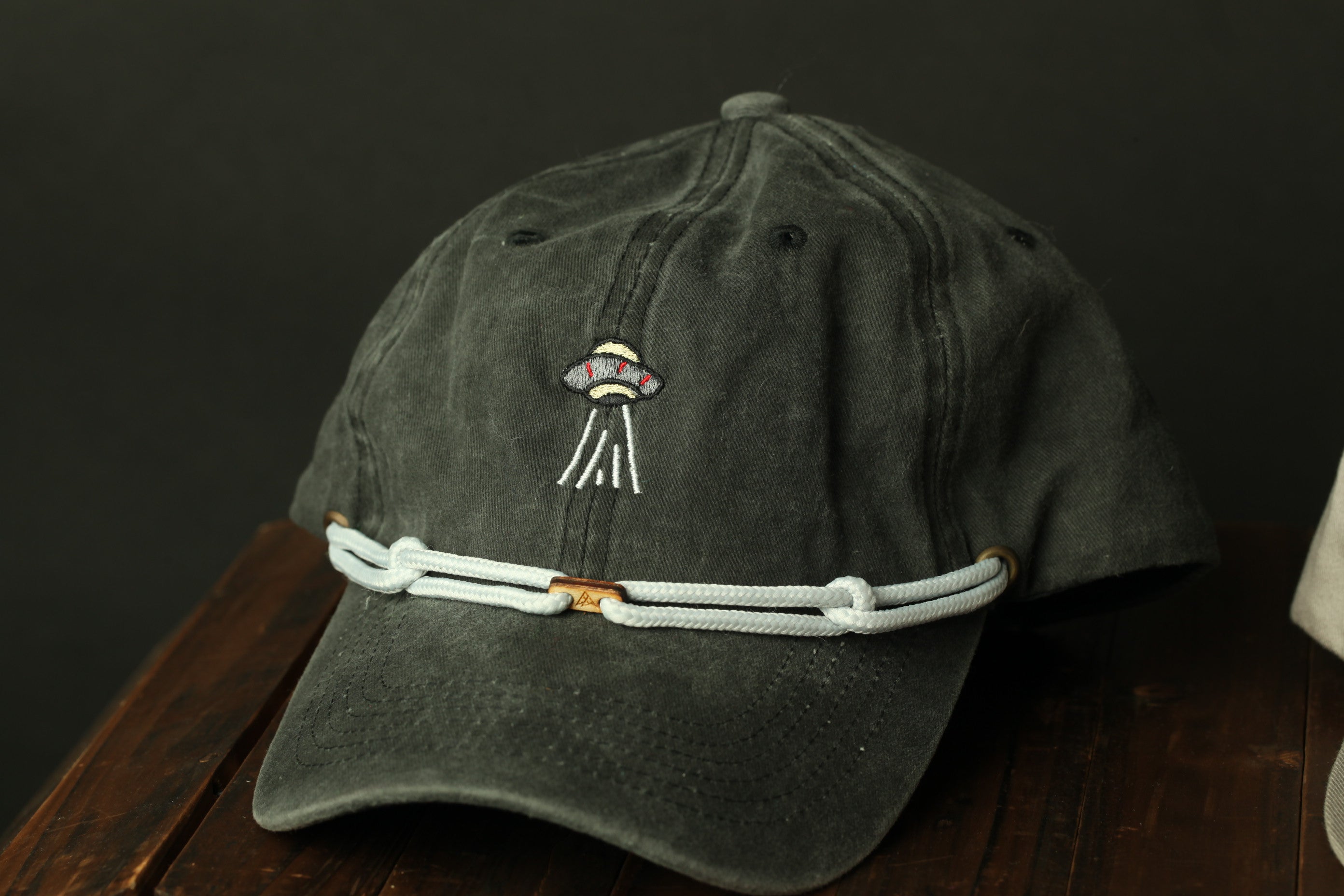 A black baseball cap with a white strap and an embroidered alien design on the front.