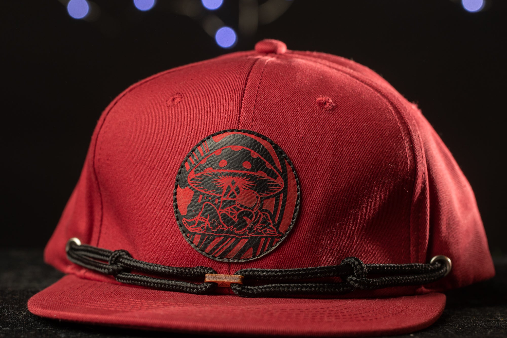 A red baseball cap with a black circular patch featuring a mushroom design.
